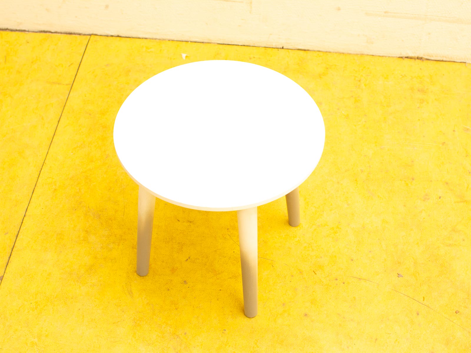 Minimalist round white table on vibrant yellow floor, perfect for home or café settings.