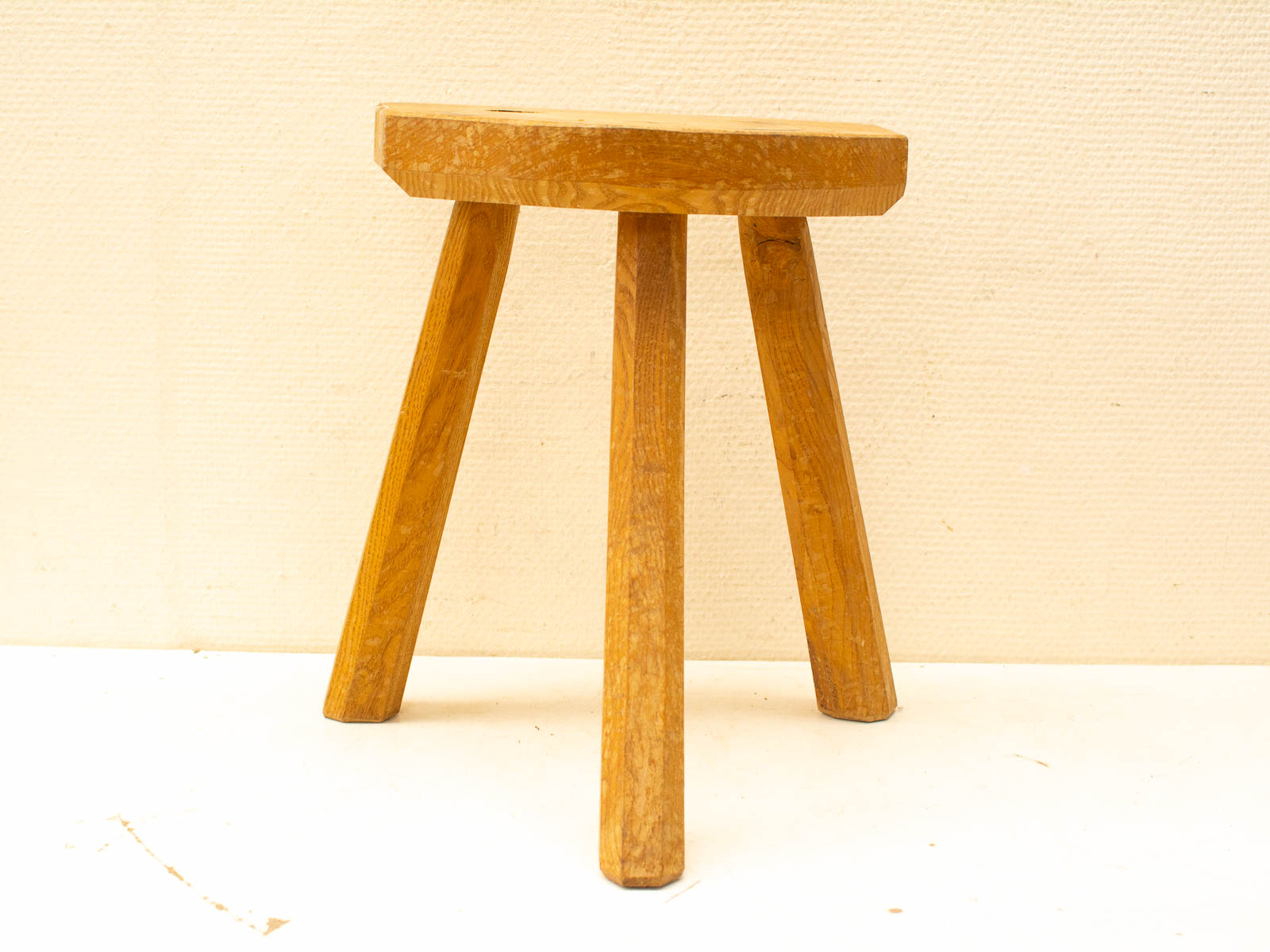 Rustic wooden stool with minimalist design, featuring a round seat and sturdy tapered legs.