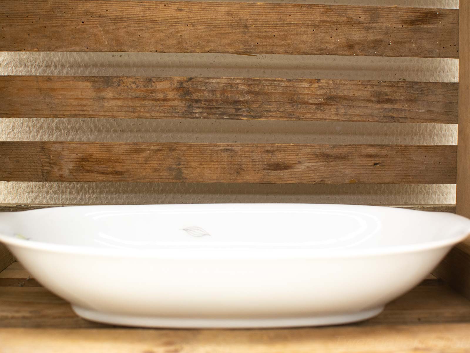 Elegant white ceramic dish on rustic wooden shelf, perfect for kitchen decor and decorative accents.