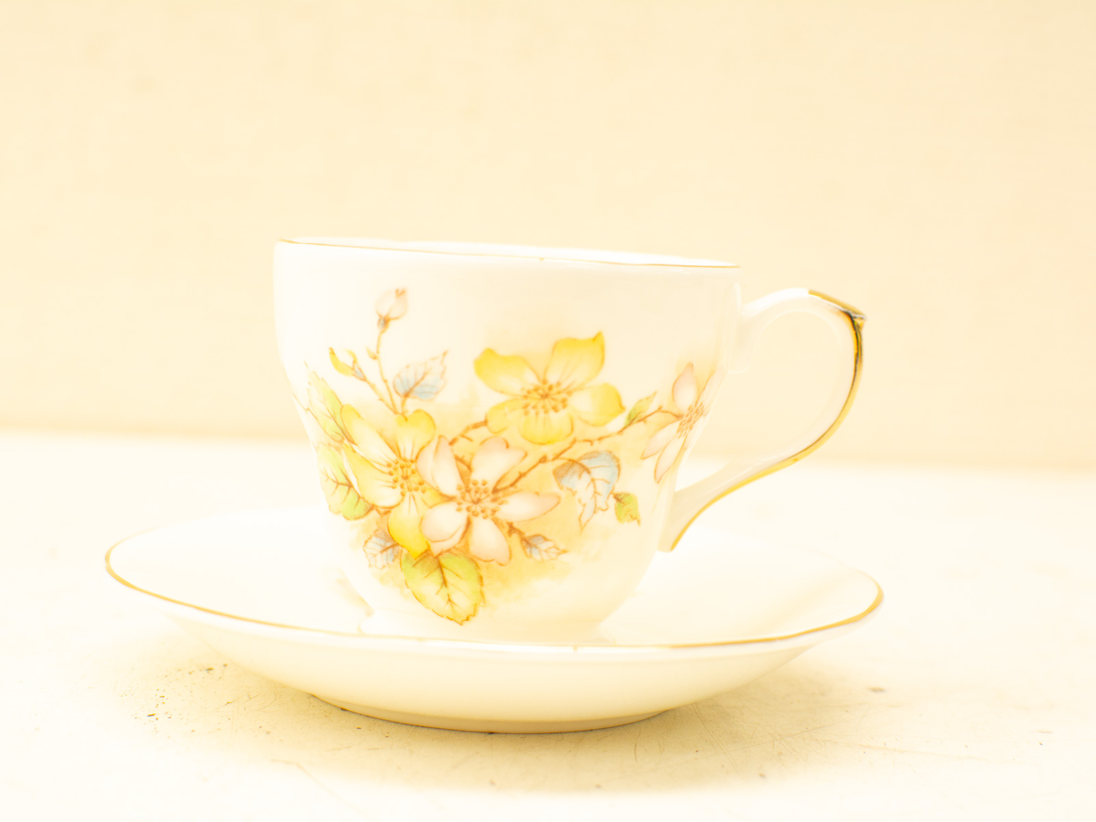 Elegant white porcelain tea cup and saucer set with yellow flowers and gold accents.