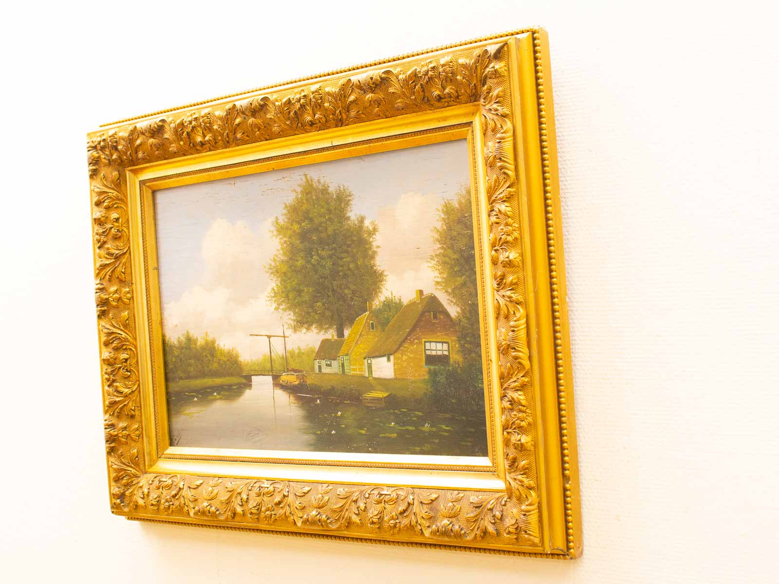 Tranquil landscape painting featuring a river, cottage, and lush greenery in an ornate frame.