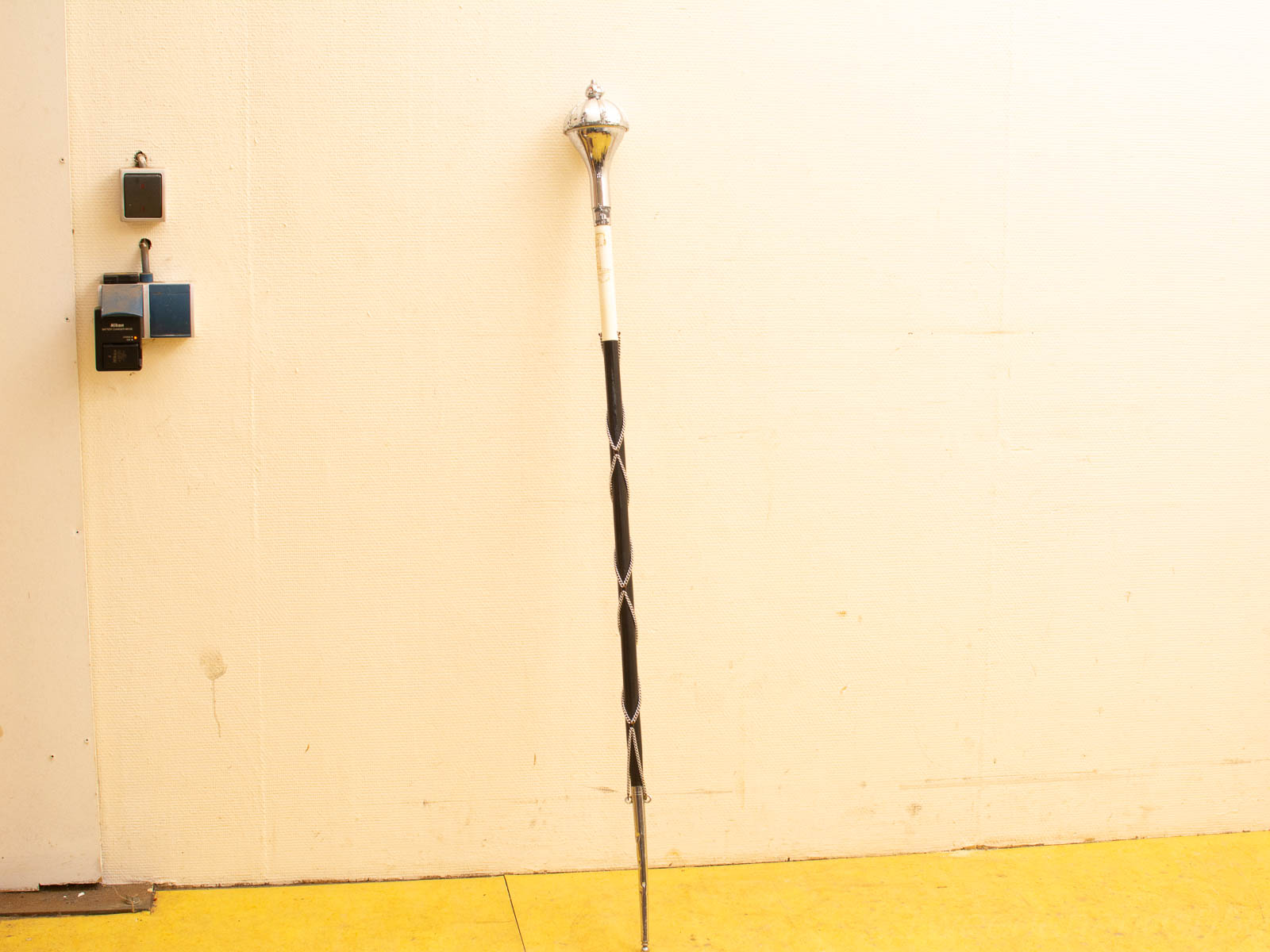 Elegant ceremonial staff with silver finial and black spiral against vibrant yellow floor.