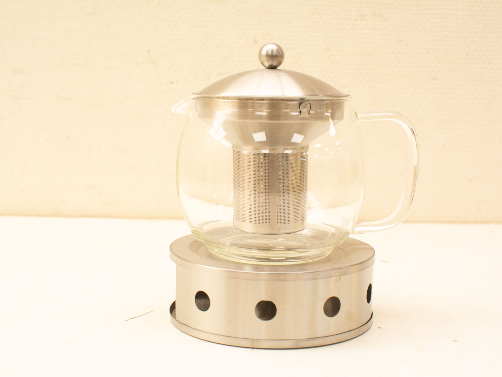 Stylish glass teapot with stainless steel infuser on a sleek metallic base for refined tea brewing.