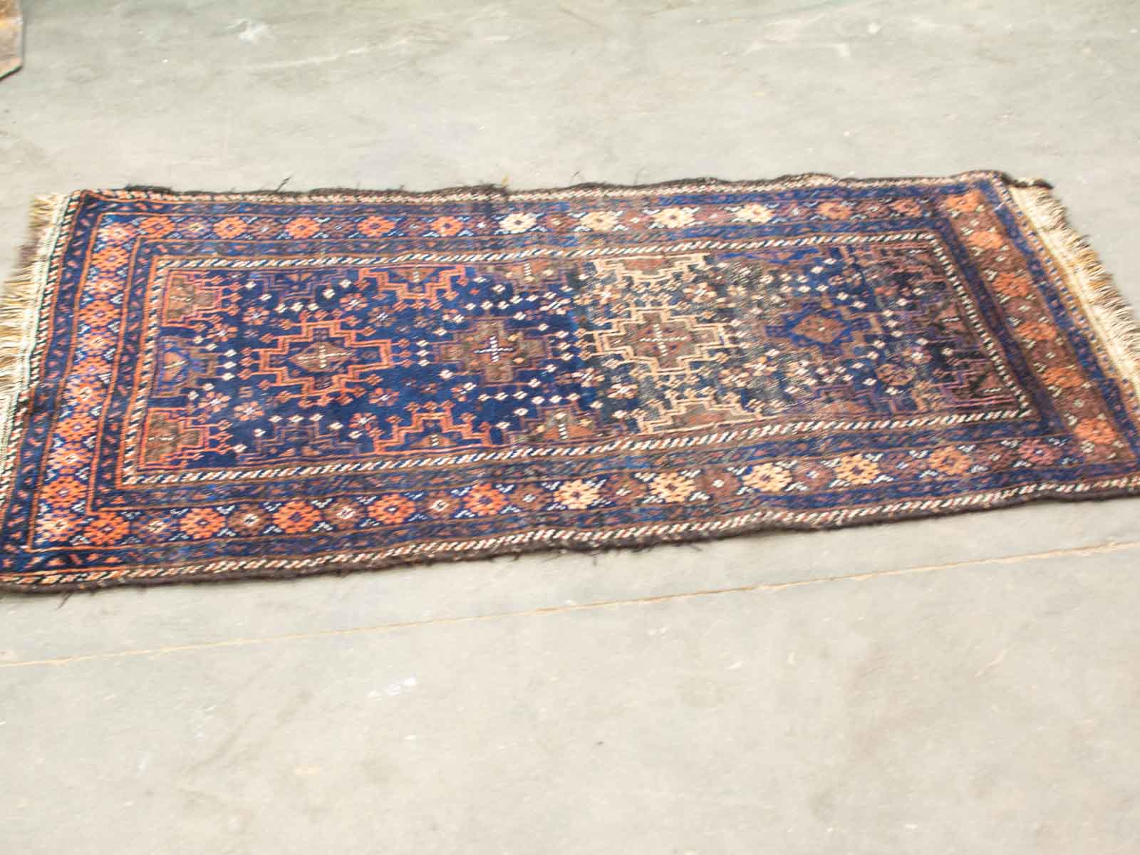 Vintage deep blue rug with intricate geometric patterns in earthy orange and brown tones.