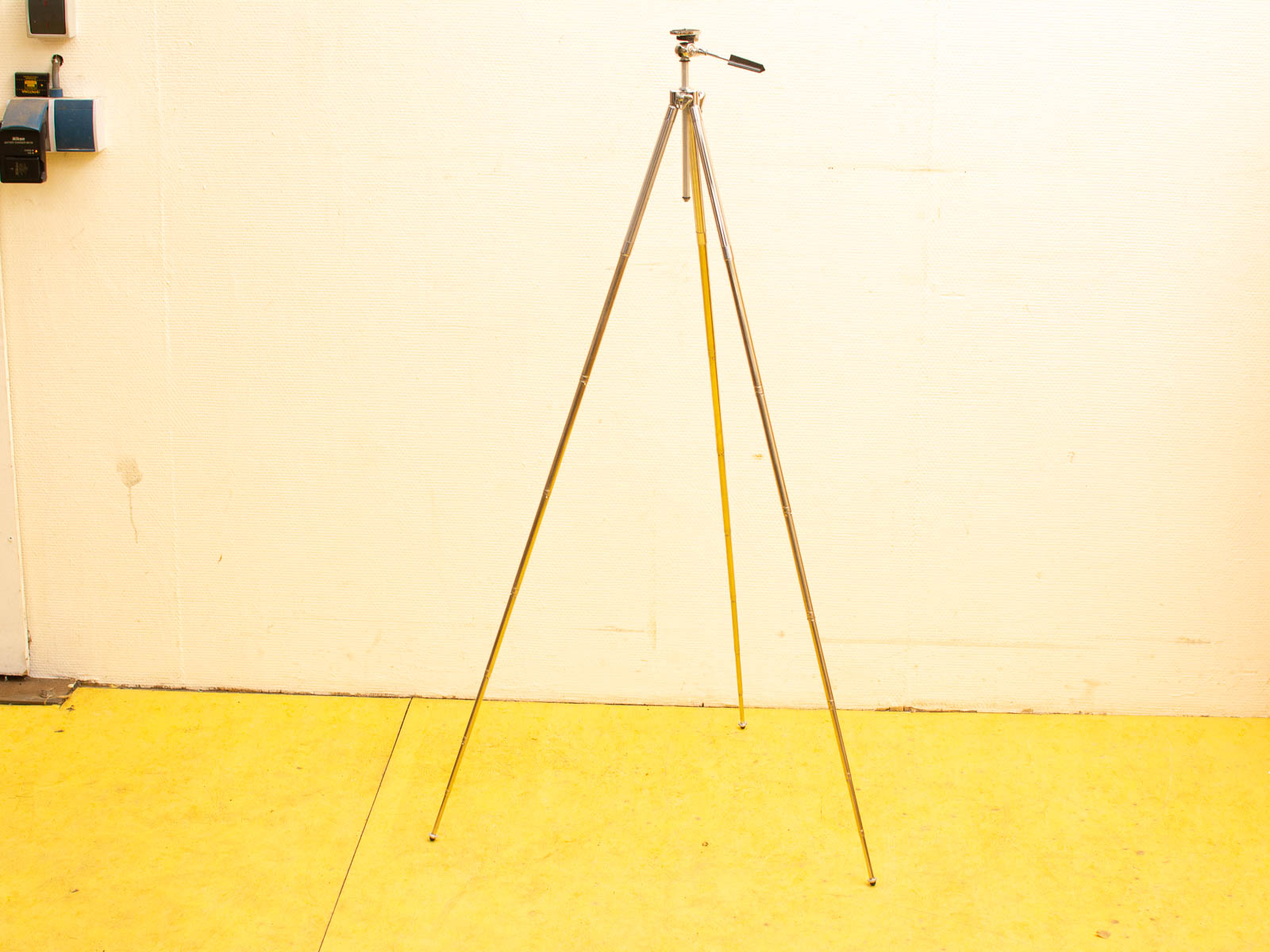 Sleek metallic tripod on vibrant yellow floor, perfect for photography and equipment support.