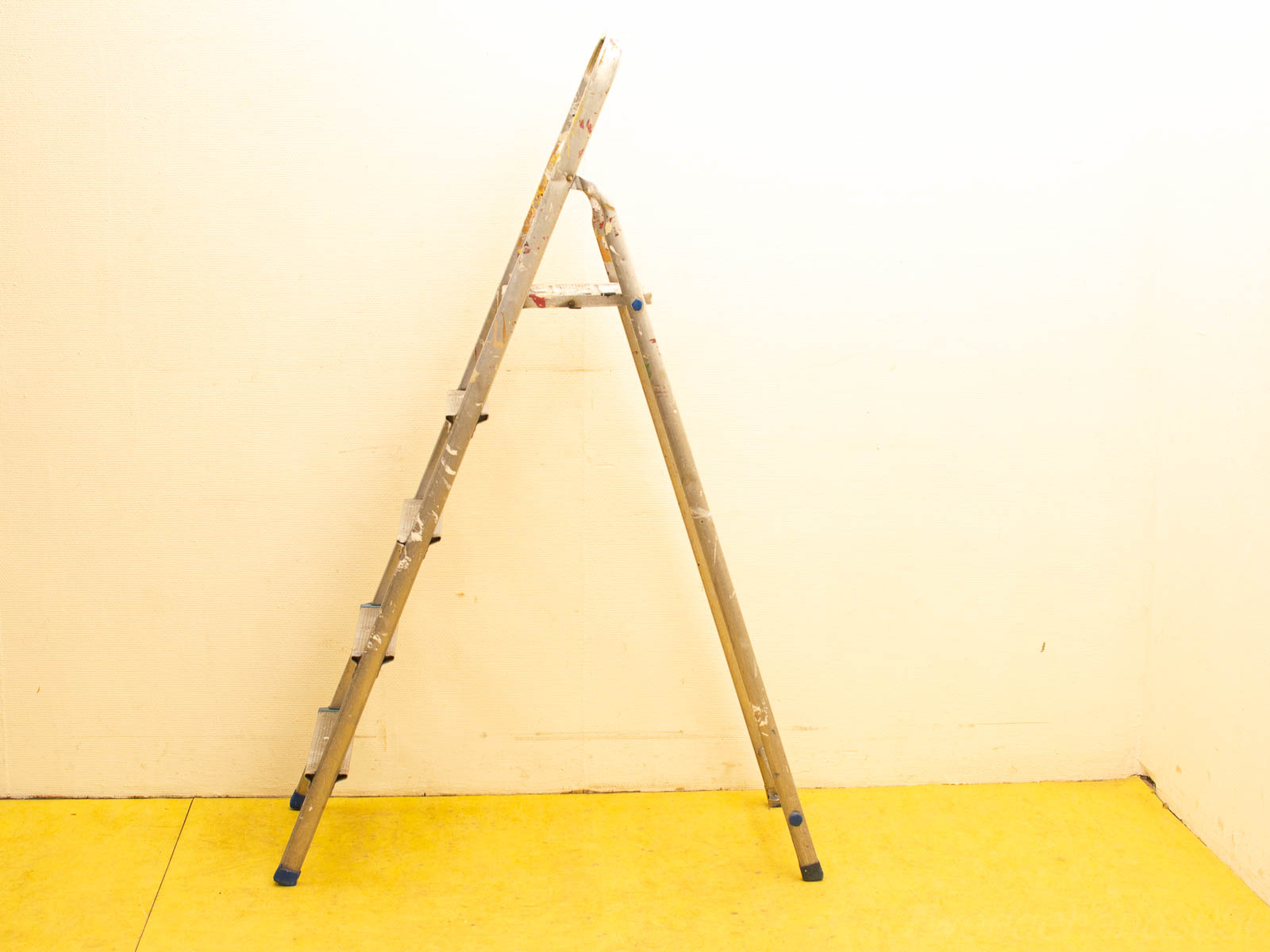 Vintage aluminum ladder with wear, showcasing functionality against a bright yellow floor.