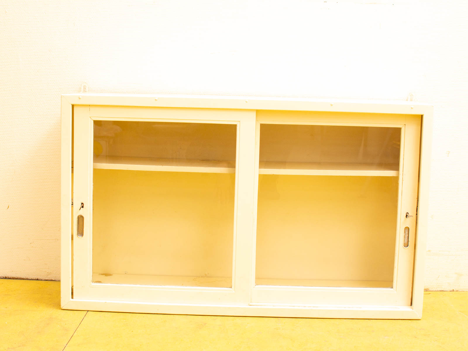 Charming vintage yellow display cabinet with glass doors and shelves for showcasing collectibles.