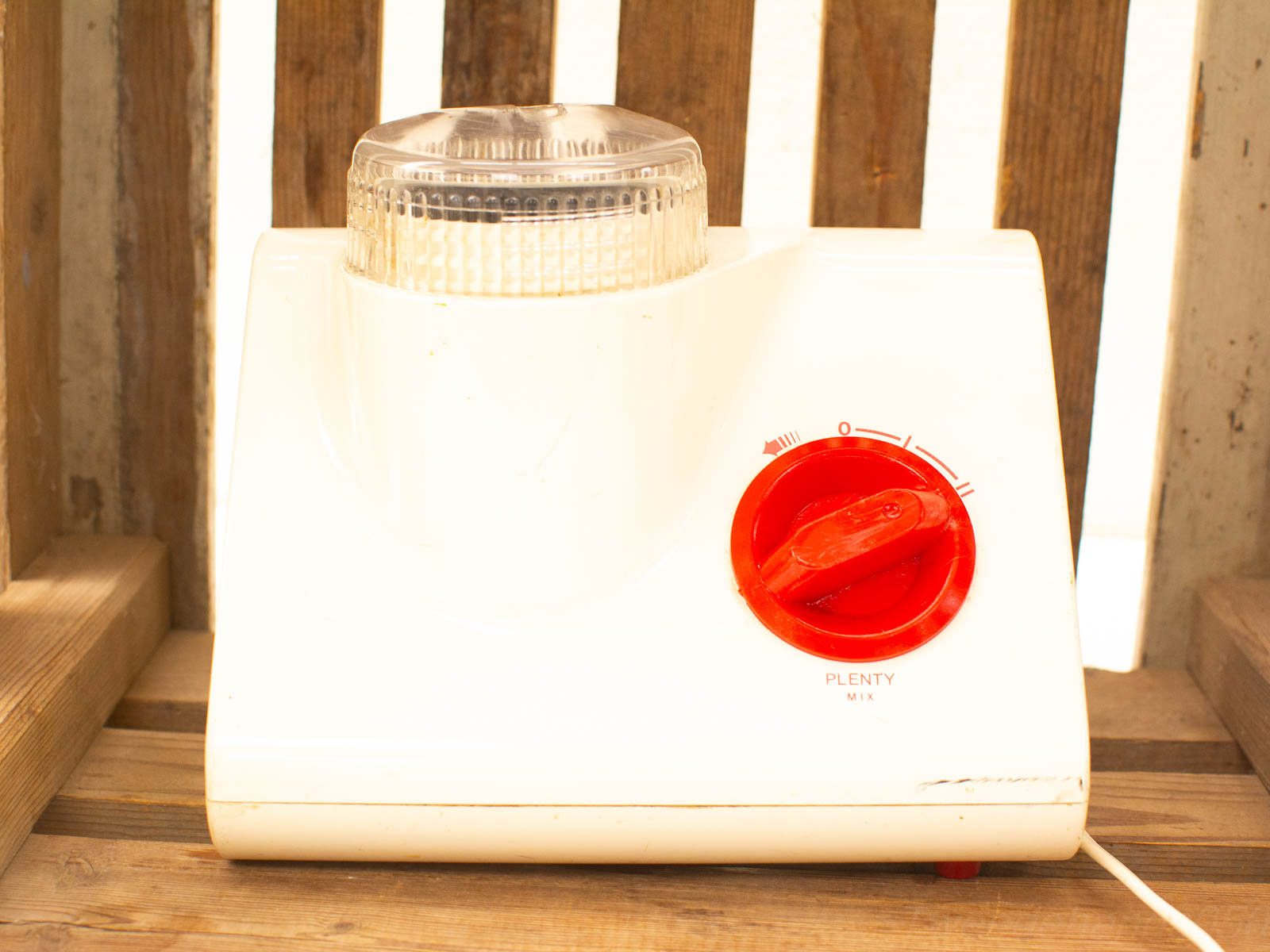 Vintage white kitchen mixer with red knob against rustic wood, perfect for nostalgic cooking.