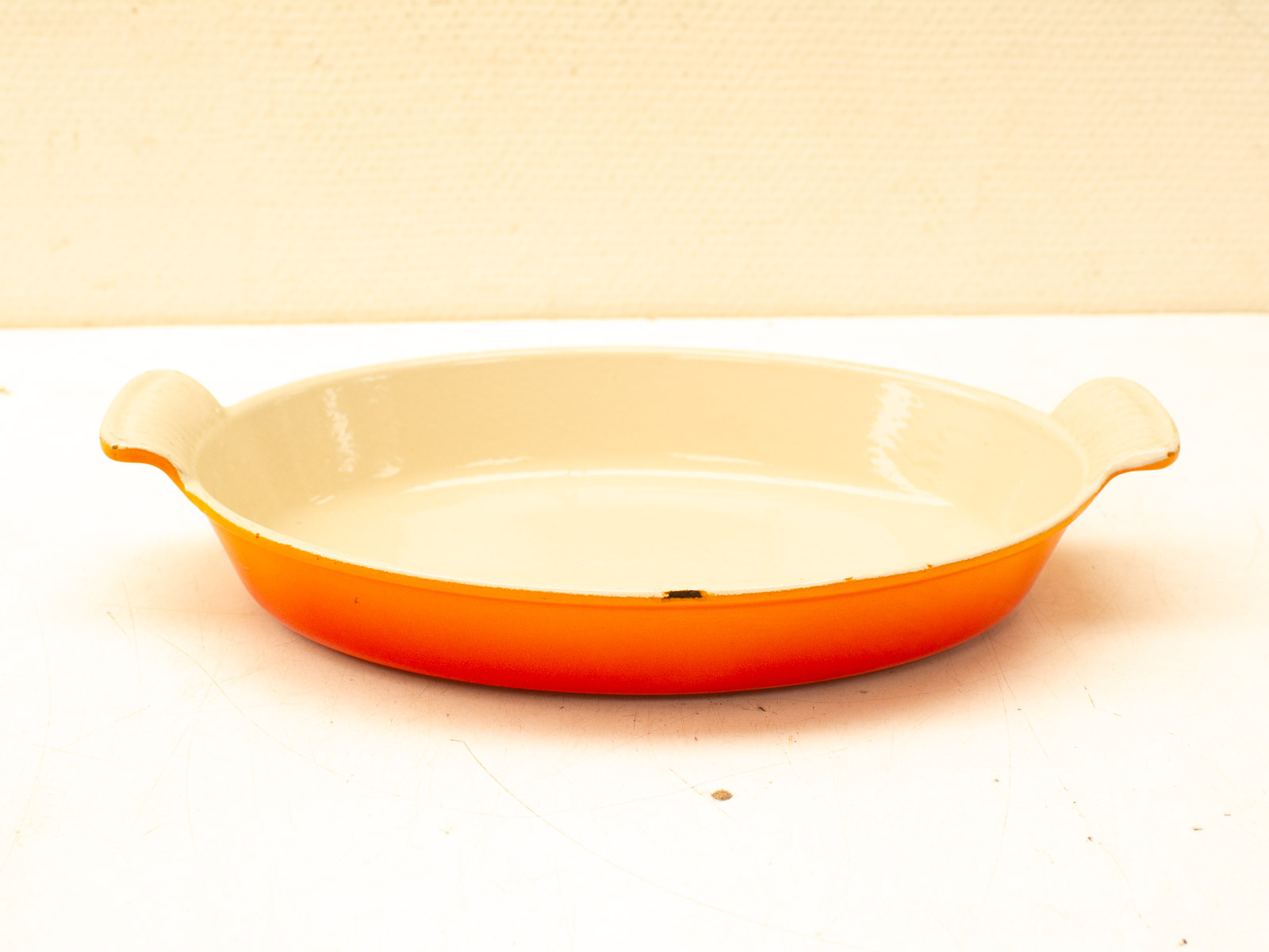 Vibrant orange gradient ceramic baking dish with cream interior and ergonomic handles for easy transport.