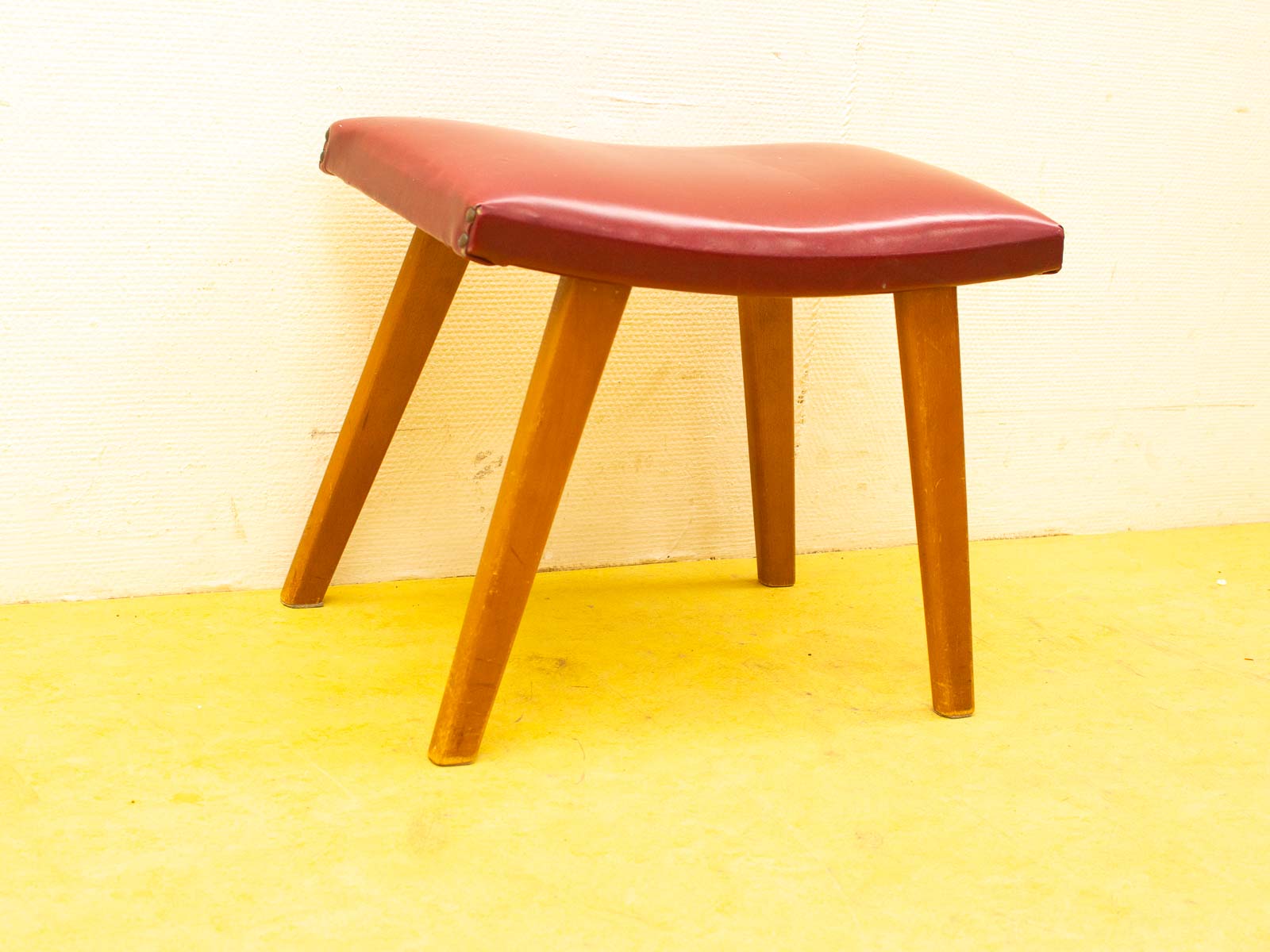 Stylish burgundy stool with wooden tapered legs, perfect for modern and inviting spaces.