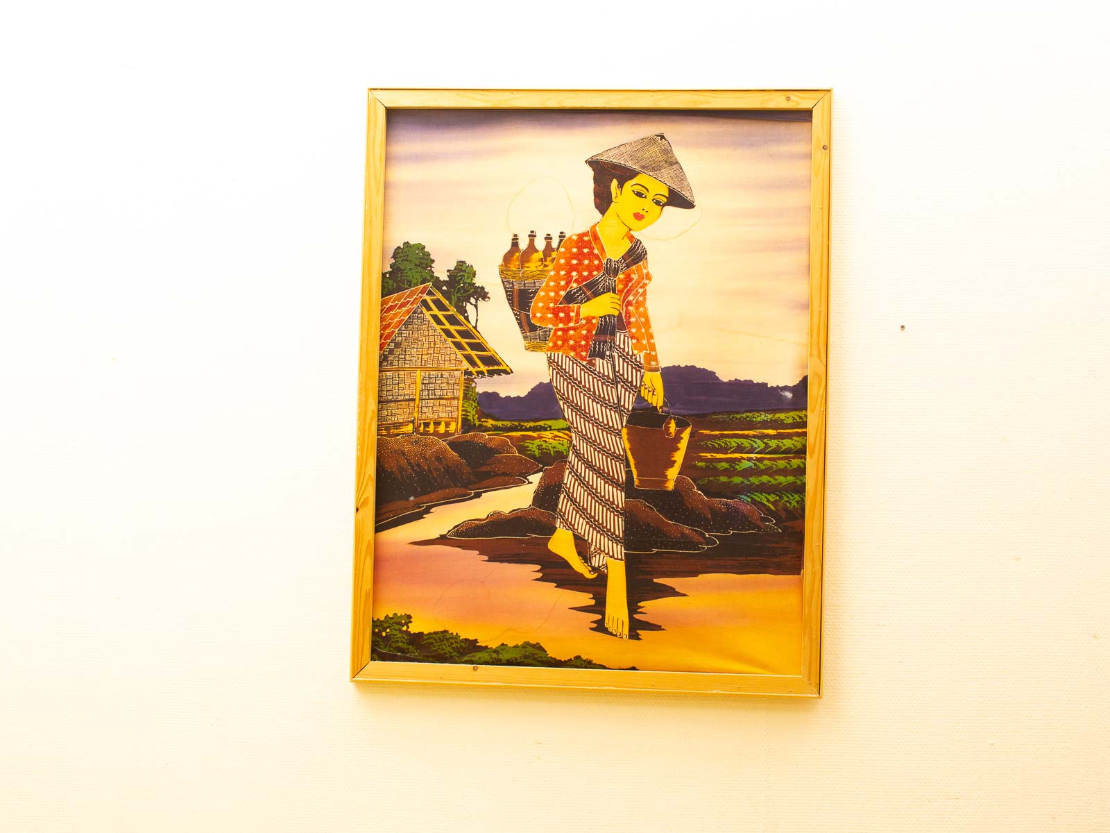 Woman in traditional dress walking a path with basket in a scenic rural landscape.