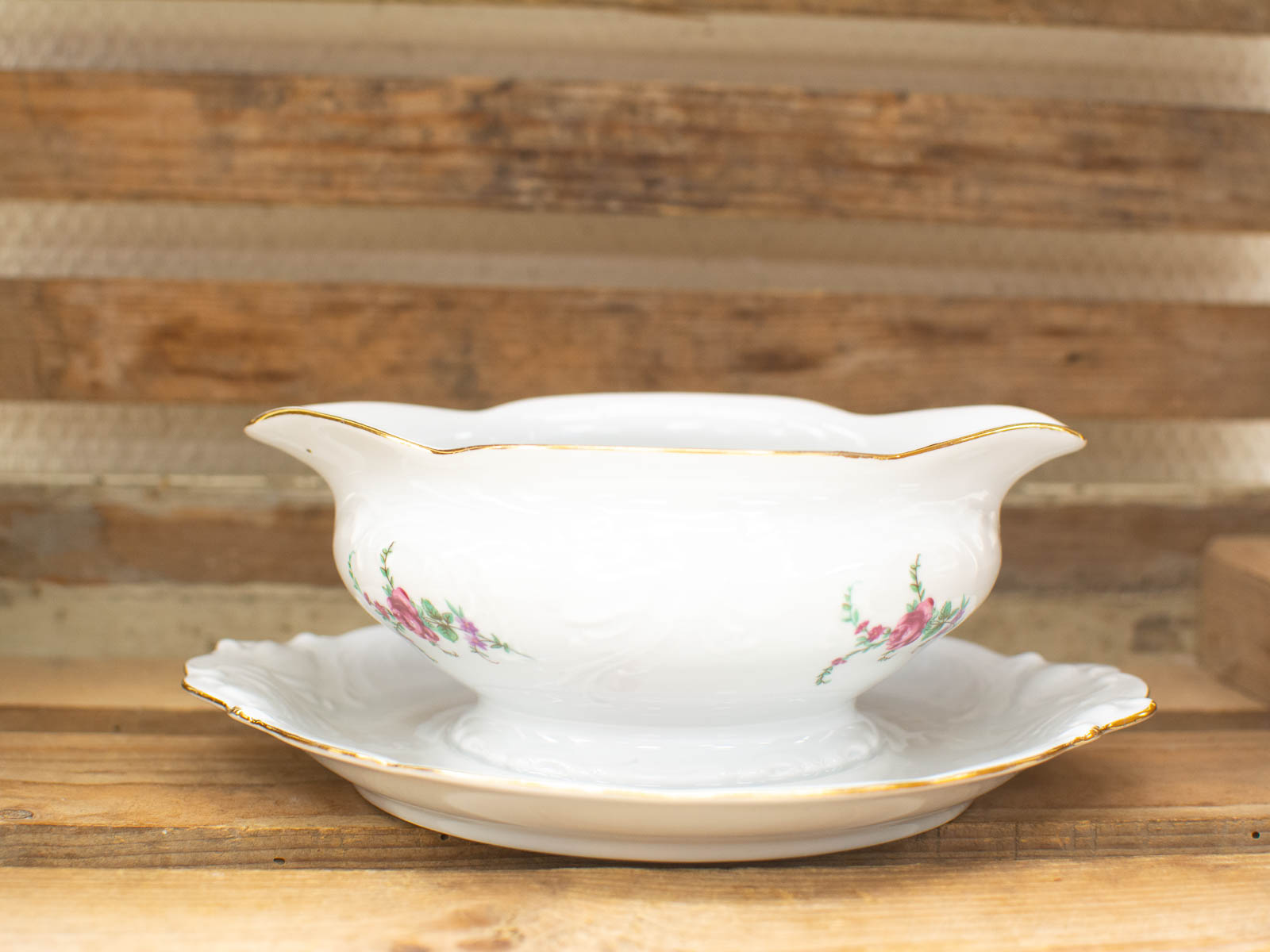 Elegant porcelain gravy boat with floral design and gold trim on rustic wood background.