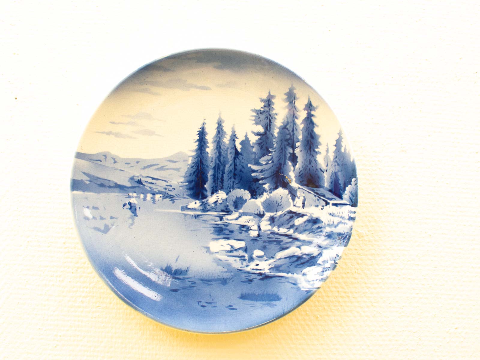 Serene blue landscape plate with hills, water, and greenery, merging art and nature beautifully.