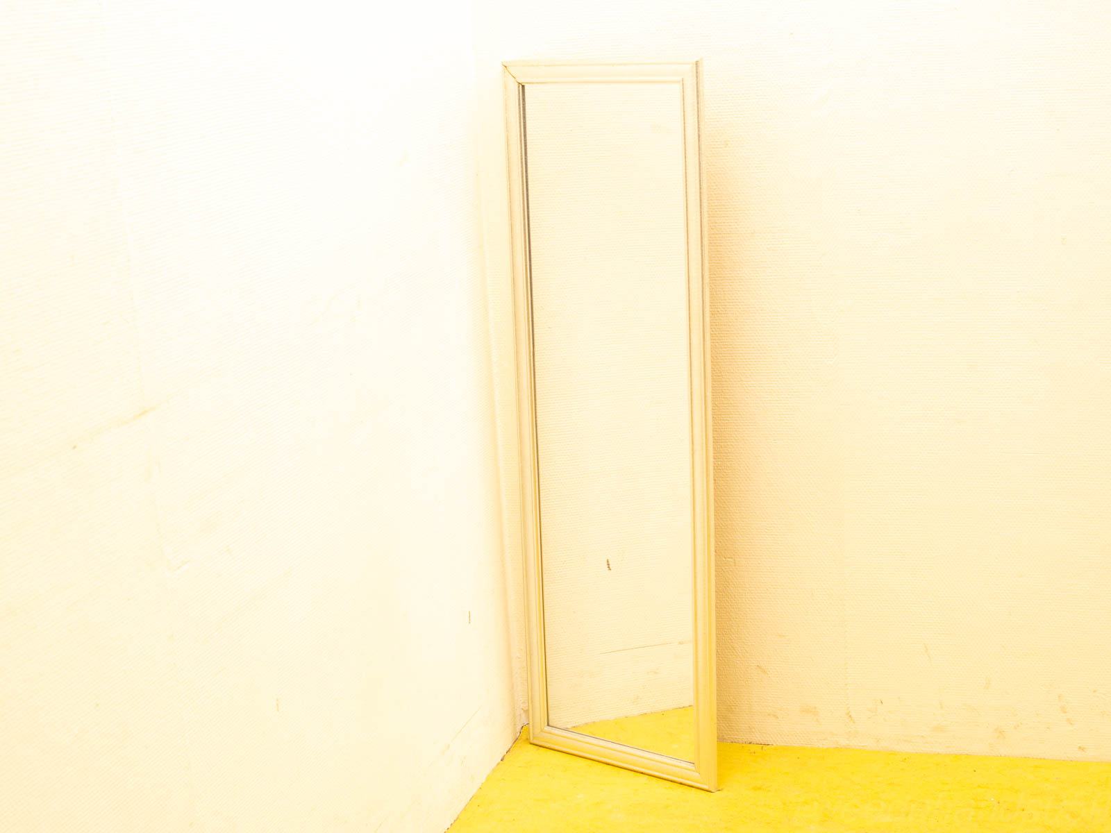 Elegant corner mirror enhances a bright room with yellow floor and soft cream walls.