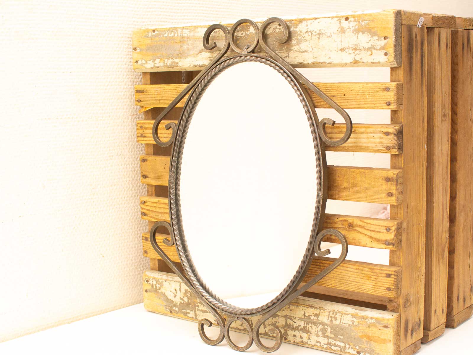 Elegant vintage oval mirror with artistic frame against rustic reclaimed wood backdrop.