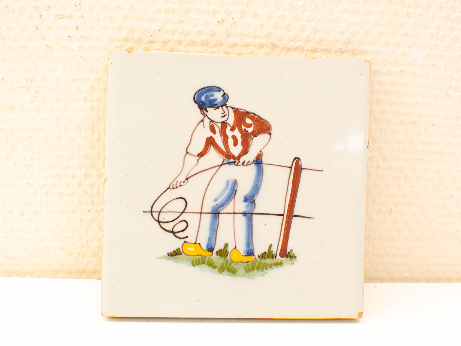 Rural life tile featuring a man winding wire on a fence post, celebrating hard work.