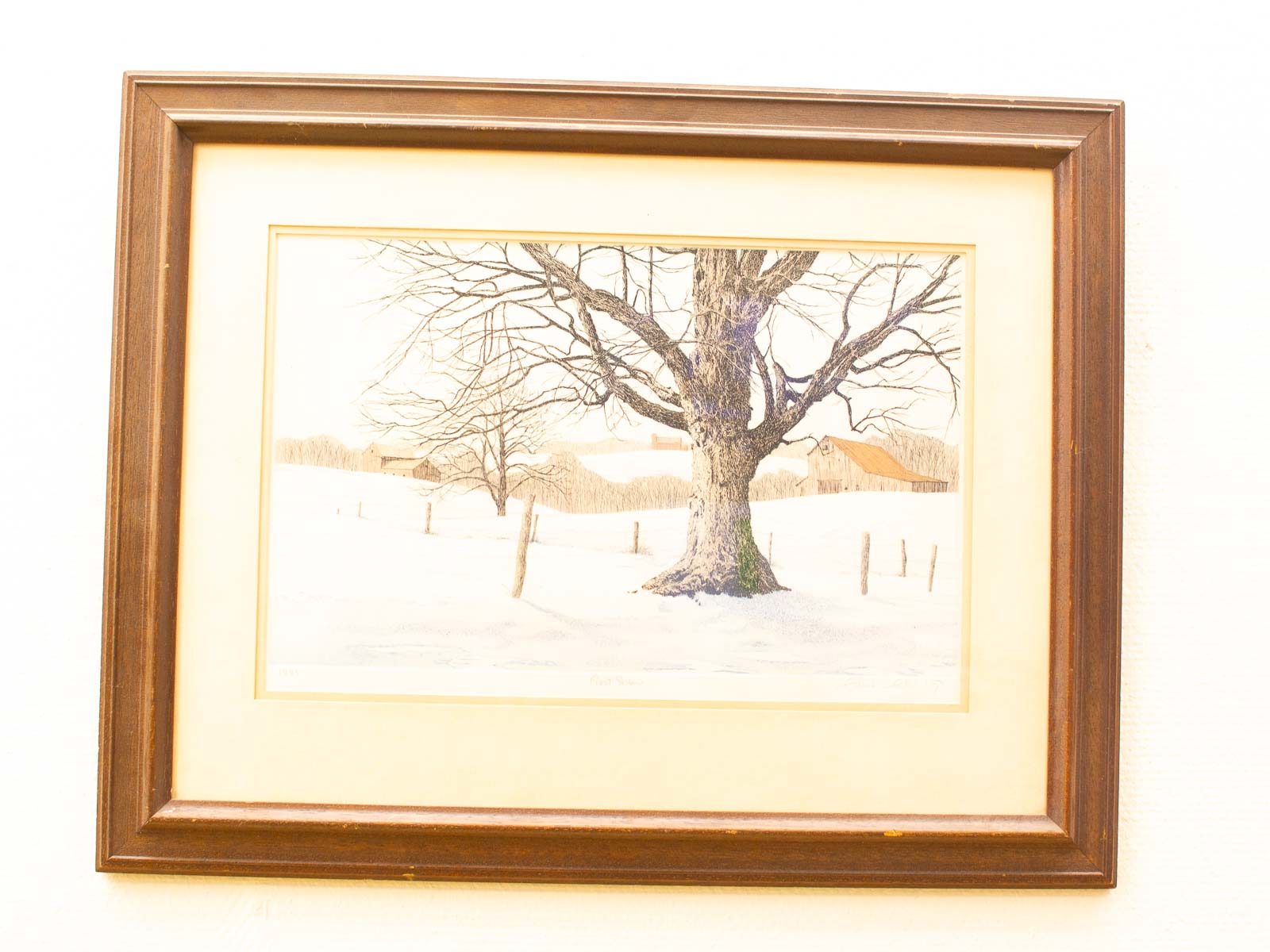 Tranquil winter landscape with a silhouetted tree, rustic buildings, and snowy fields.