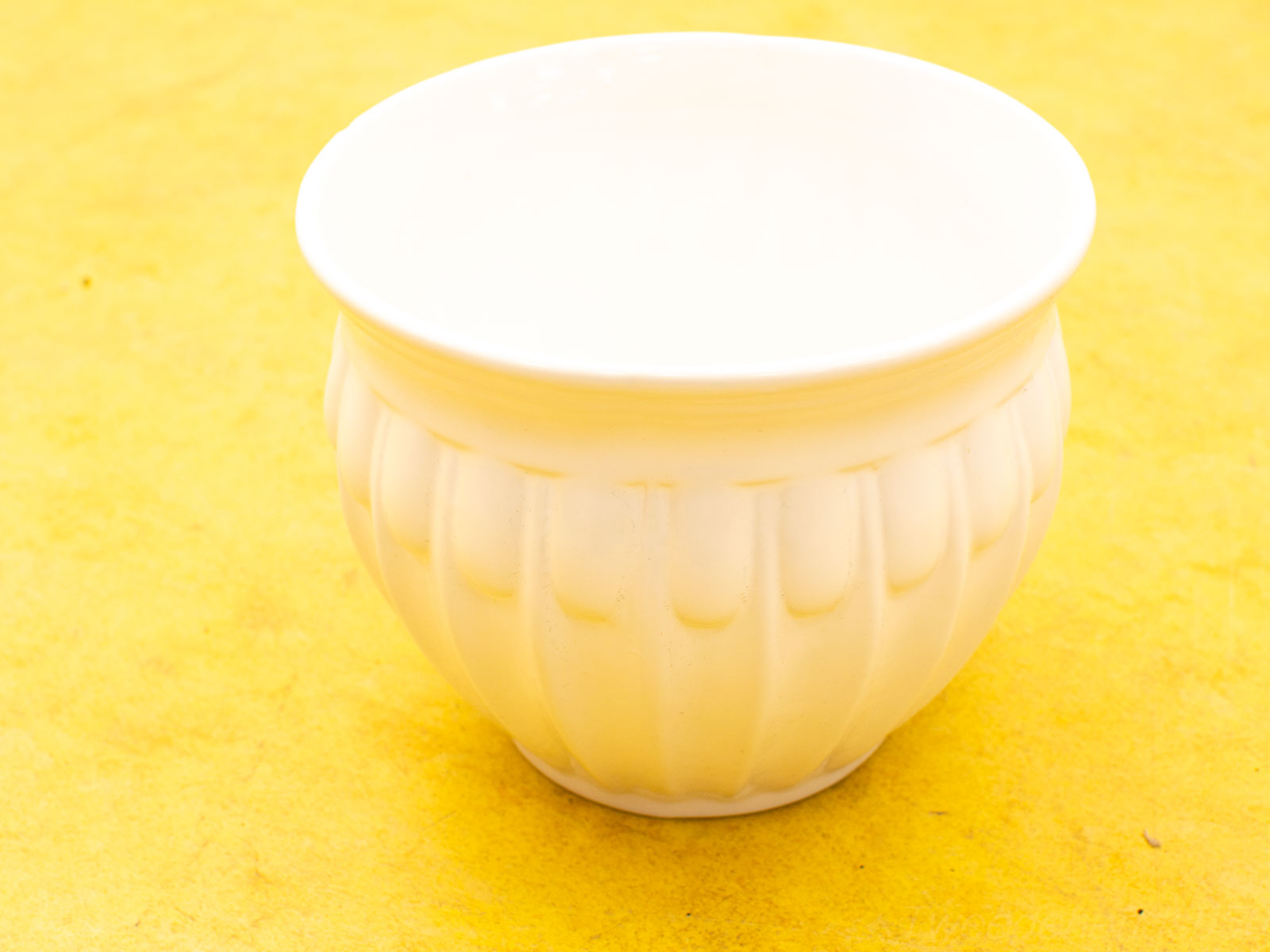 Elegant white ceramic bowl against a cheerful yellow background, perfect for serving or decoration.