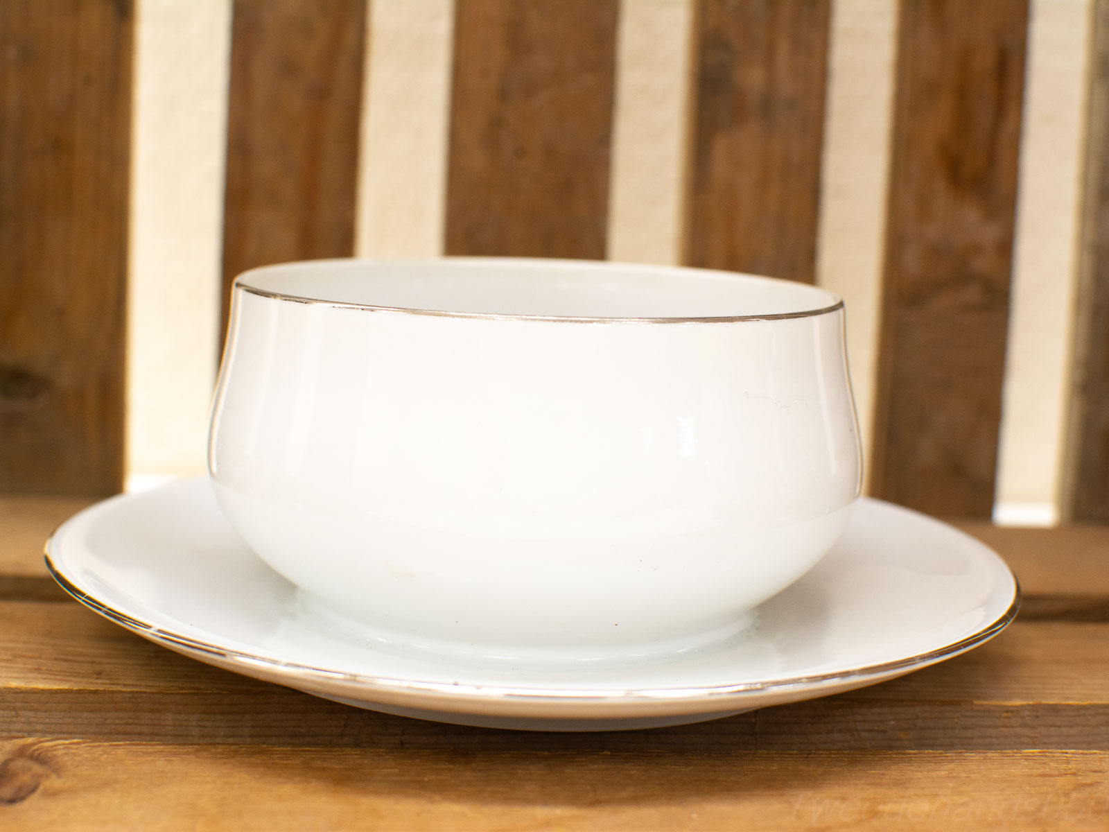 Elegant white porcelain bowl with gold trim on matching plate against rustic wooden backdrop.