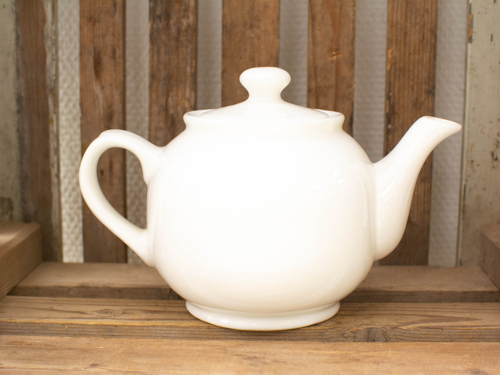 Elegant vintage white teapot on rustic wooden shelf, perfect for tea lovers and cozy gatherings.