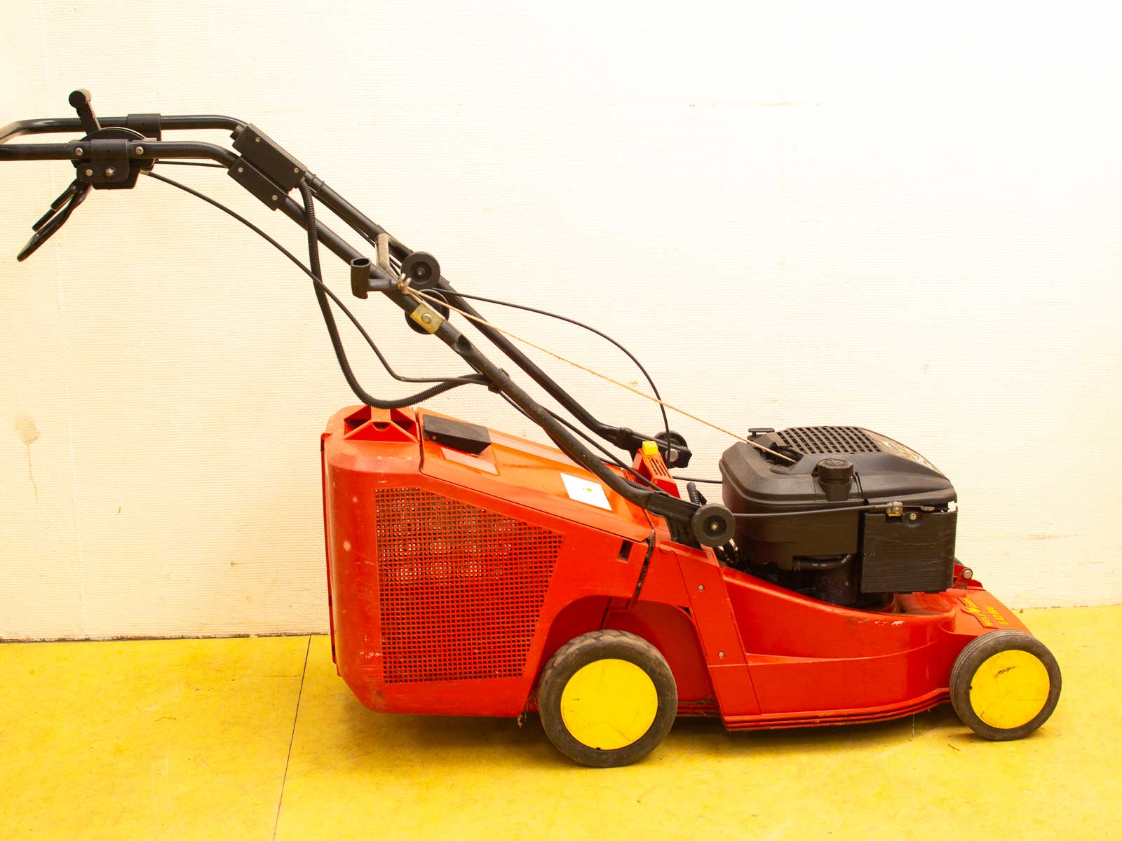 Vintage red lawn mower with yellow accents, compact design, ideal for efficient yard maintenance.