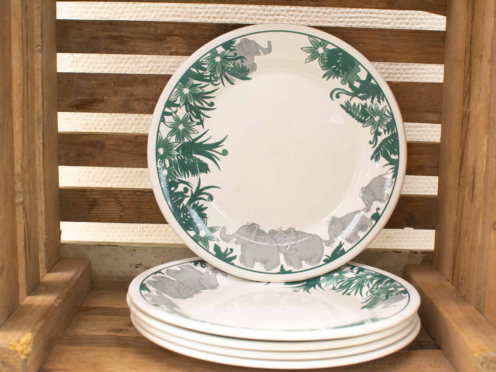 Decorative ceramic plates with hand-painted tropical elephant design stacked on a rustic wooden crate.