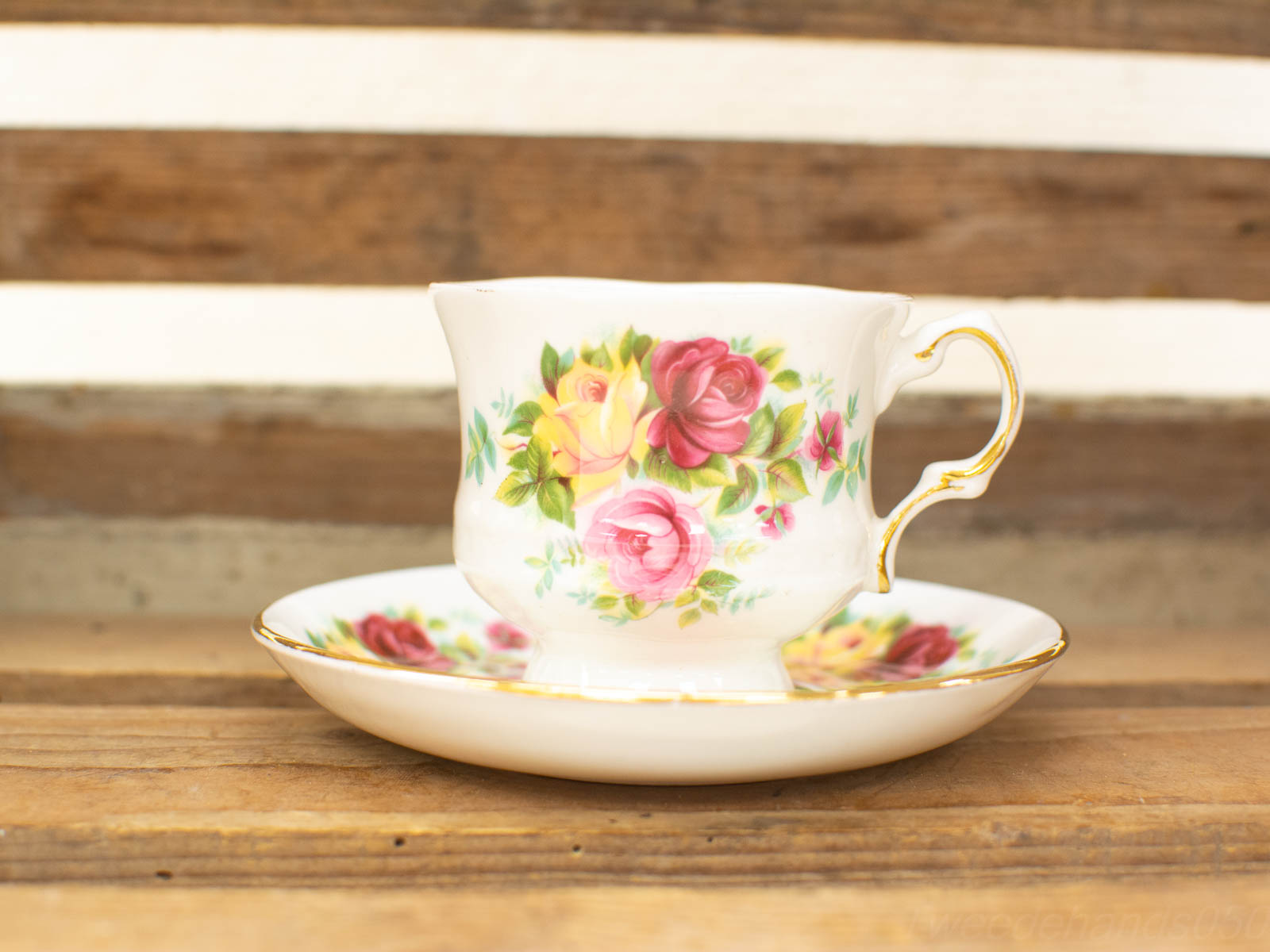 Vintage porcelain teacup and saucer with colorful floral design on rustic wooden backdrop.