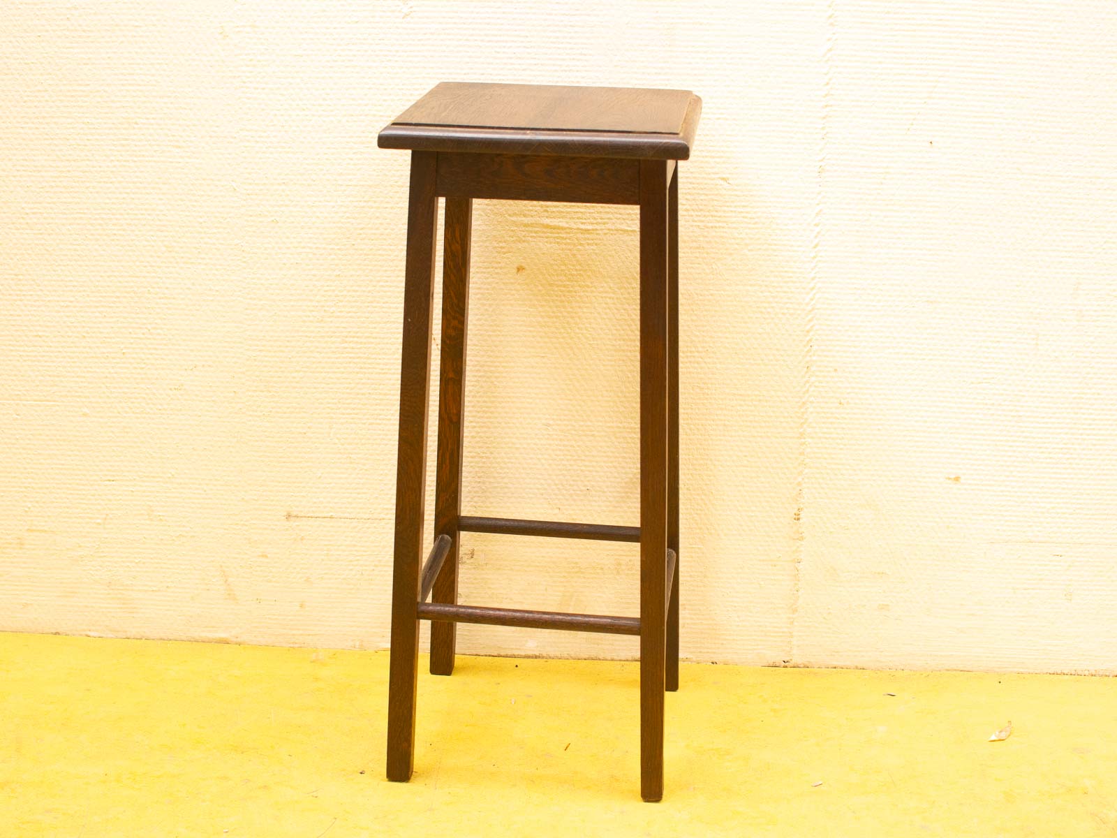 Elegant wooden stool with a minimalist design, dark finish, and tapered legs for versatile use.