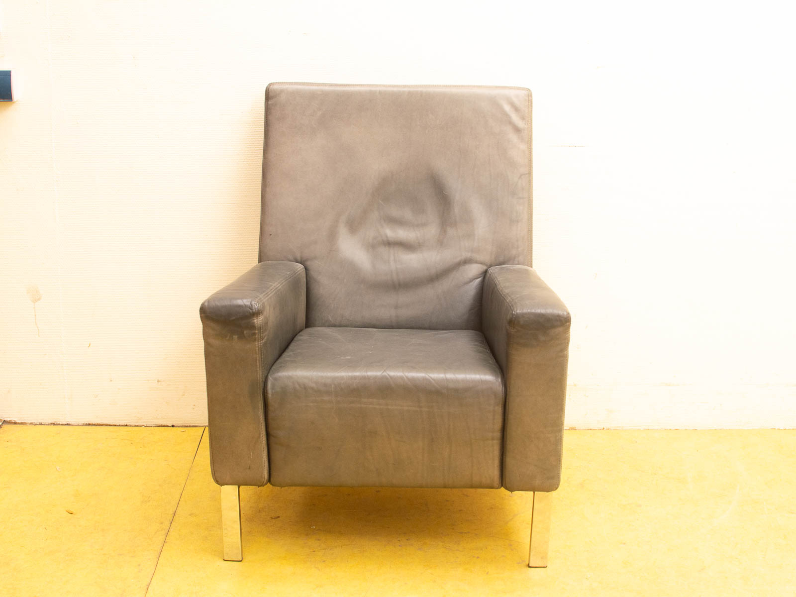 Minimalist gray leather armchair with high backrest and metal legs, perfect for modern interiors.