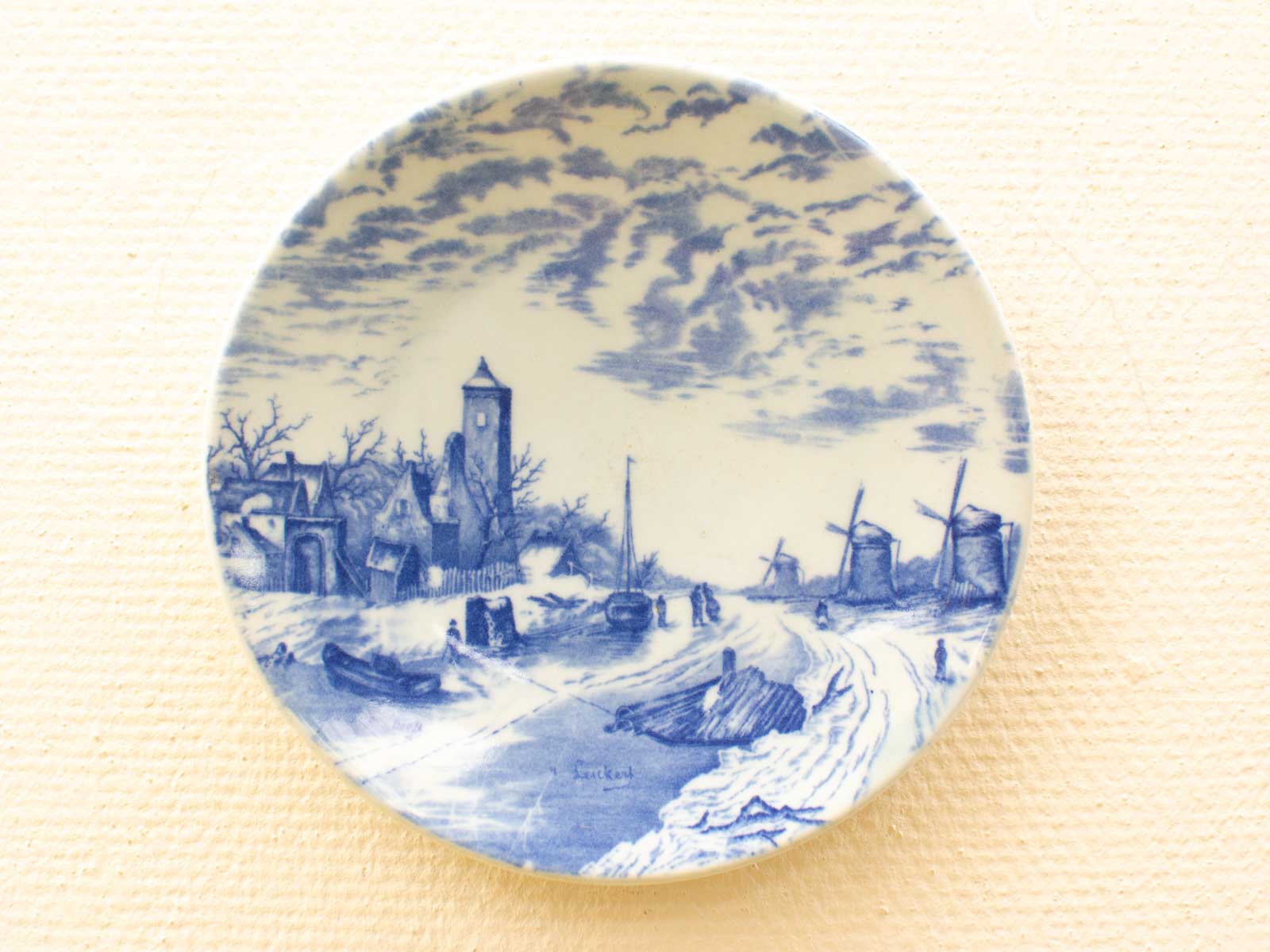 Winter landscape porcelain plate featuring a village, clock tower, and windmills in blue and white.