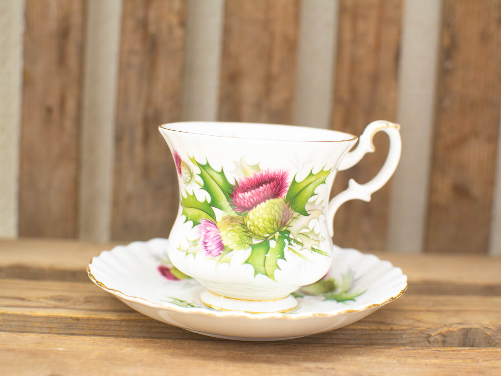 Vintage porcelain teacup set with vibrant thistle motif on rustic wood backdrop.