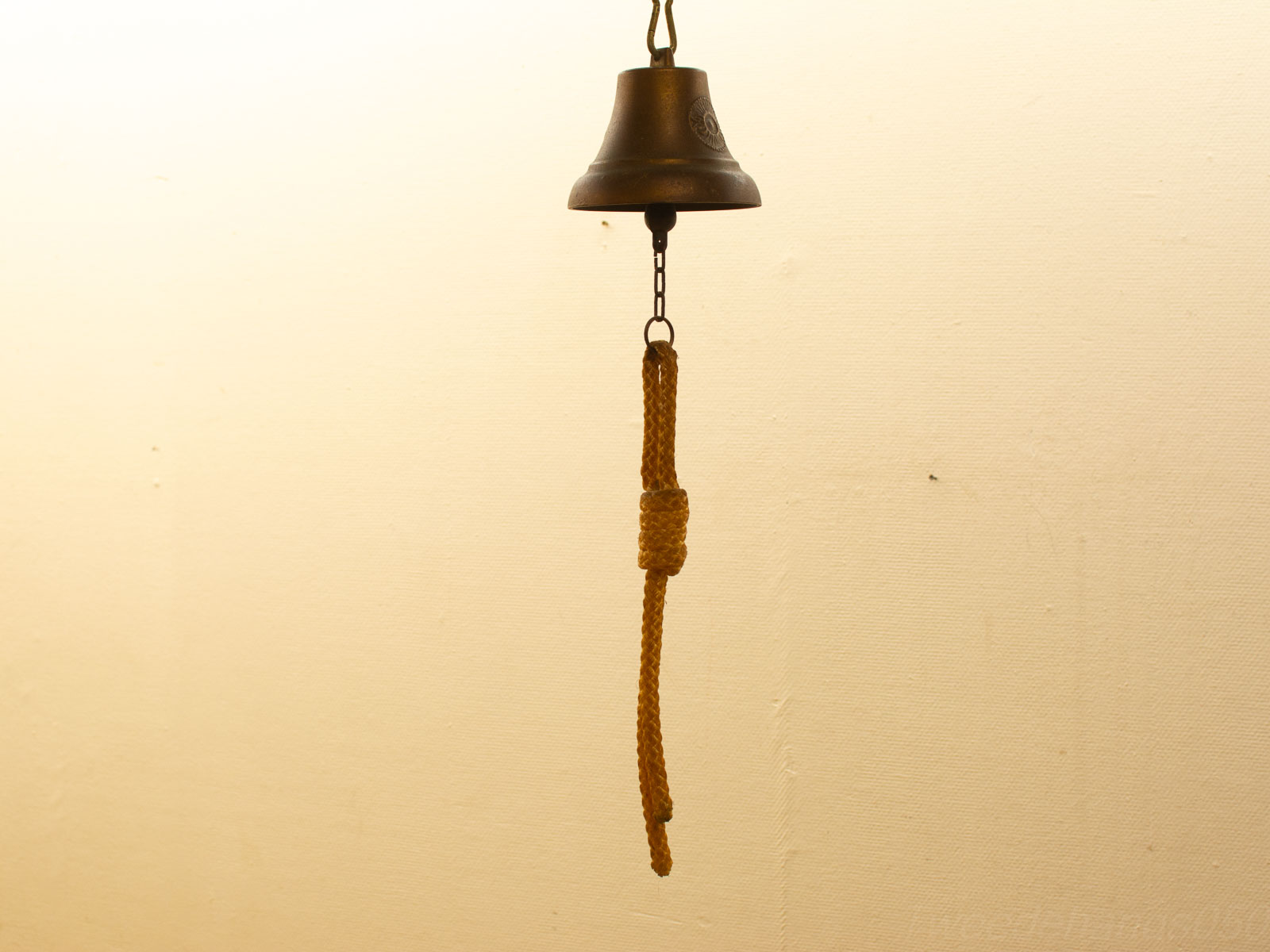 Vintage brass bell with chain and rope against a serene, textured wall.