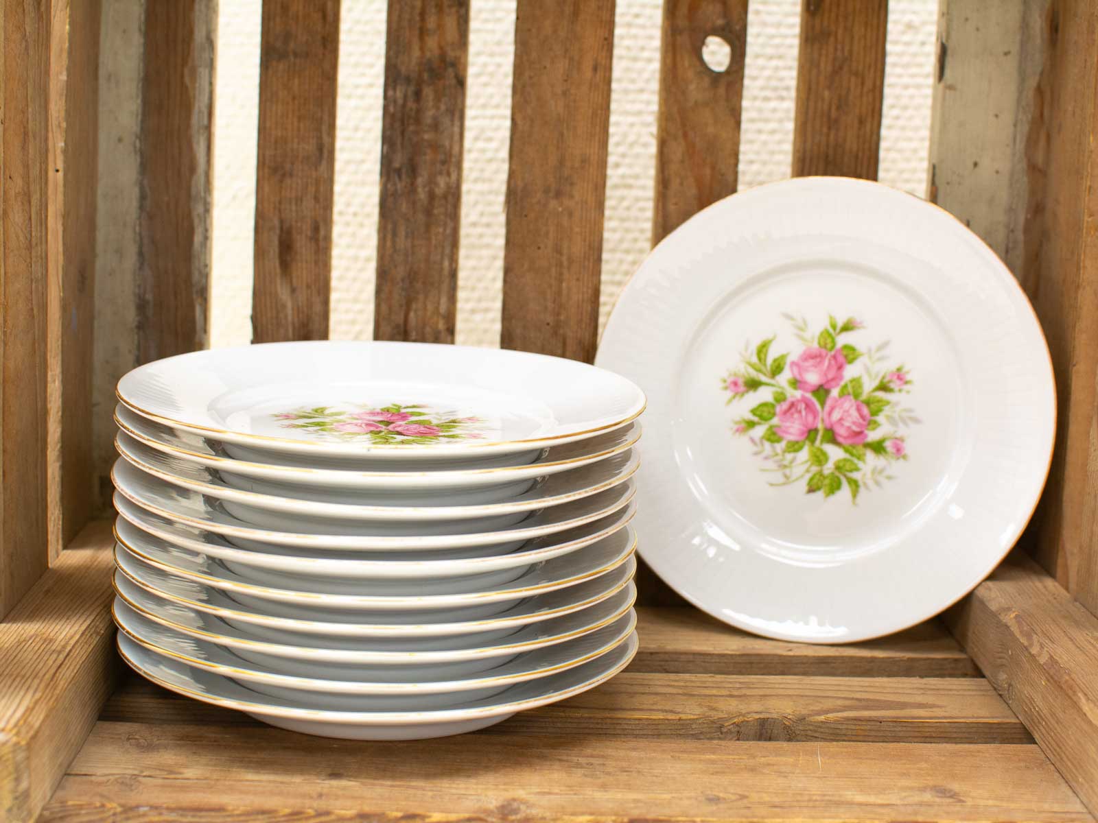 Elegant porcelain plates with rose designs in a rustic wooden crate, perfect for special occasions.