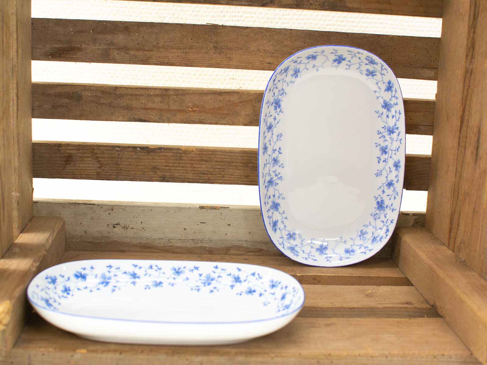 Elegant porcelain dishes with blue flowers in a rustic wooden crate, perfect for home decor.