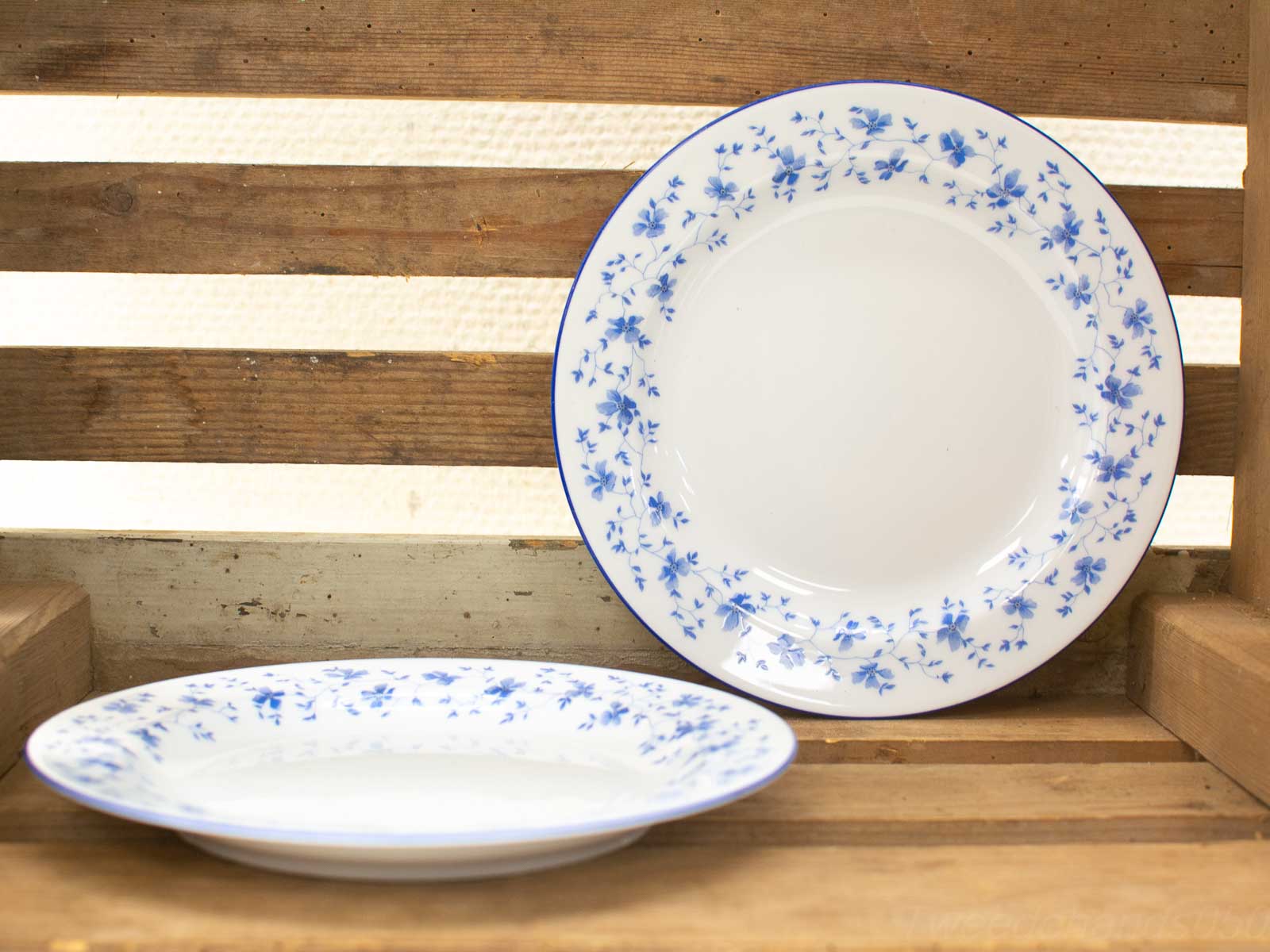 Elegant ceramic plates with blue floral designs atop a rustic wooden crate, perfect for dining.