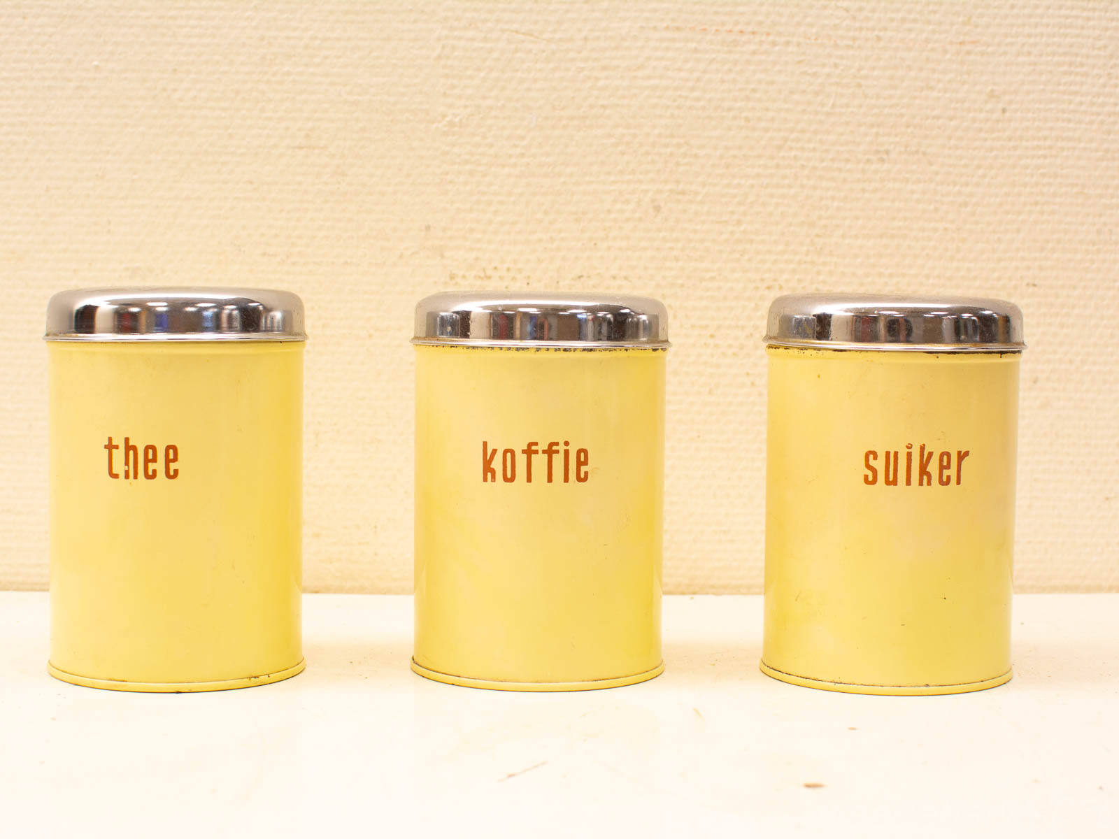 Vintage yellow Dutch canisters for tea, coffee, and sugar with a nostalgic charm.