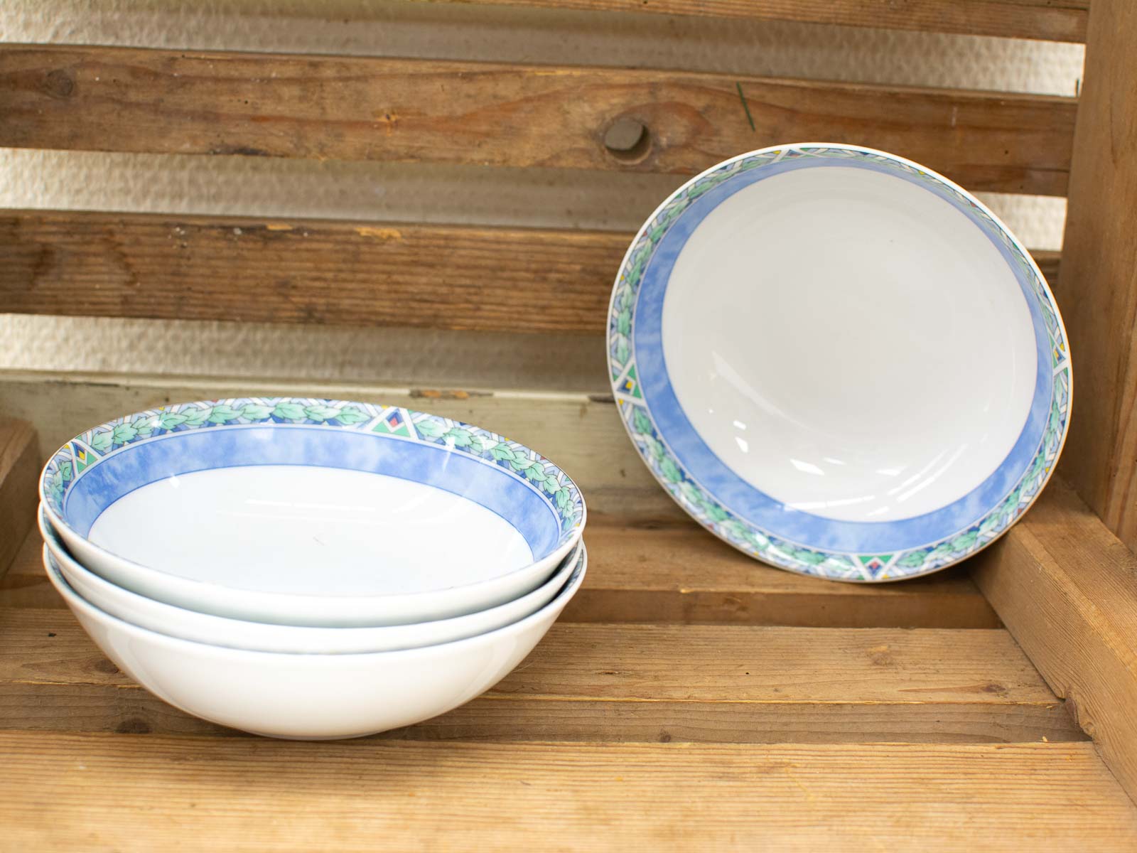 Elegant white ceramic bowls with blue and green patterns on a rustic wooden shelf.