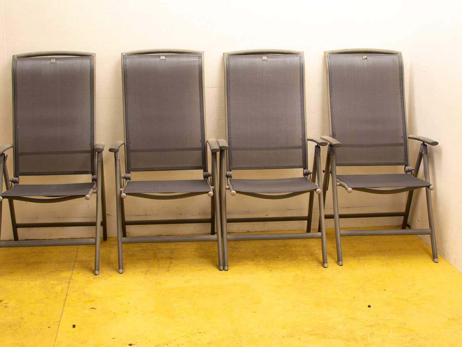 Sleek folding chairs against a plain wall with a vibrant yellow floor in a minimalist setting.