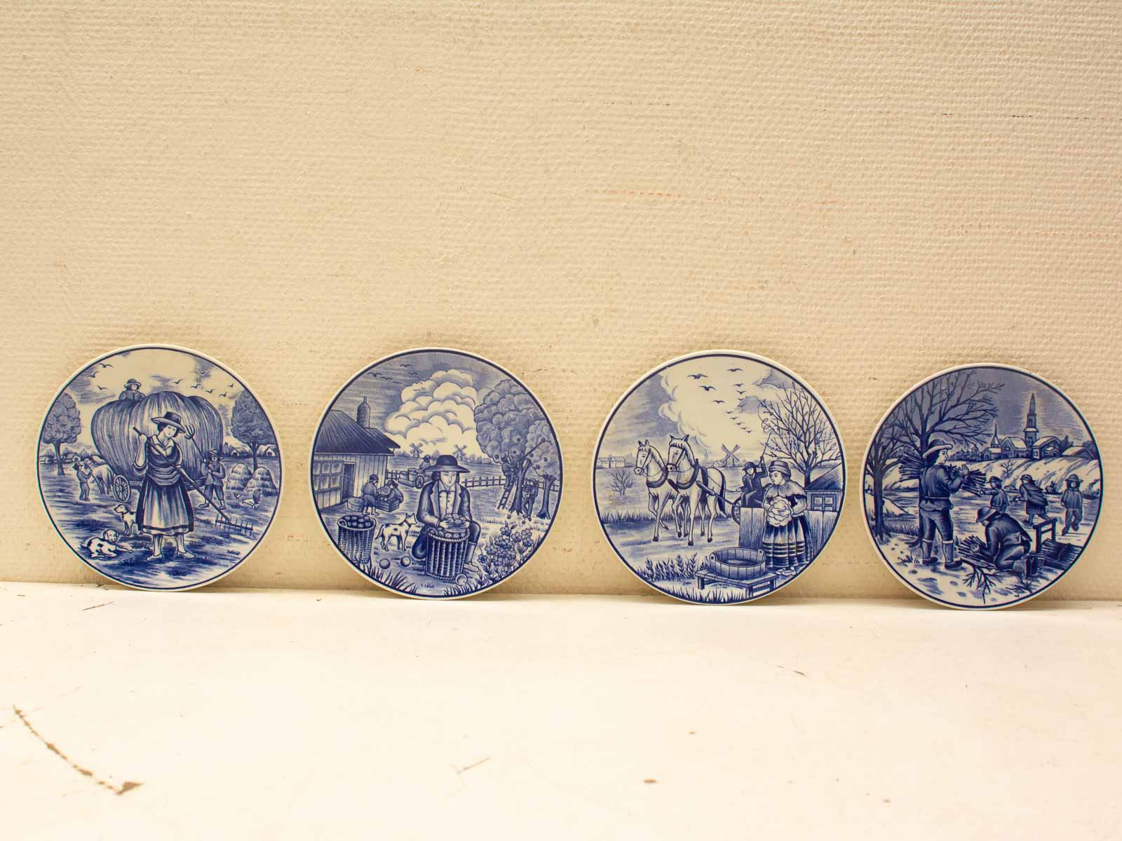 Four blue and white decorative plates showcasing traditional rural scenes and seasonal activities.