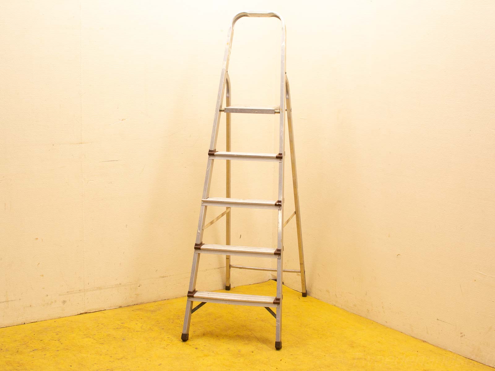 Sturdy aluminum step ladder against a beige wall, complementing a vibrant yellow floor.