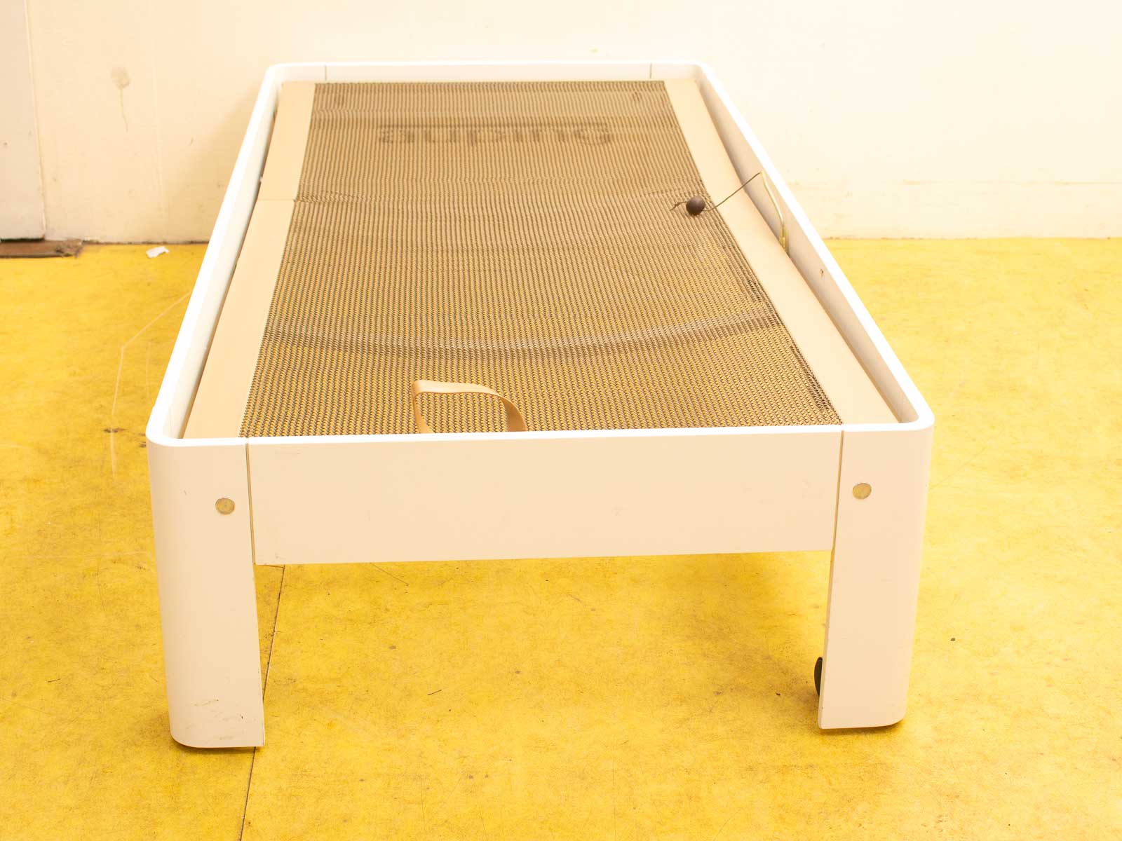 Sleek white minimalist bed frame with mesh surface and wheels for easy mobility.