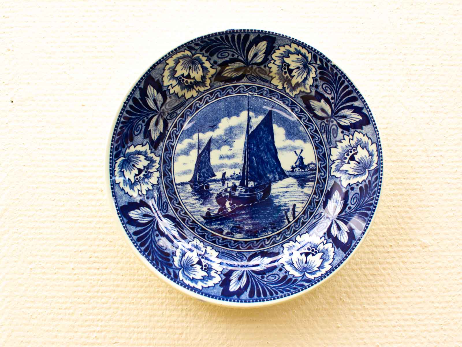 Traditional blue-white porcelain plate featuring nautical scene and floral details, celebrating maritime history.