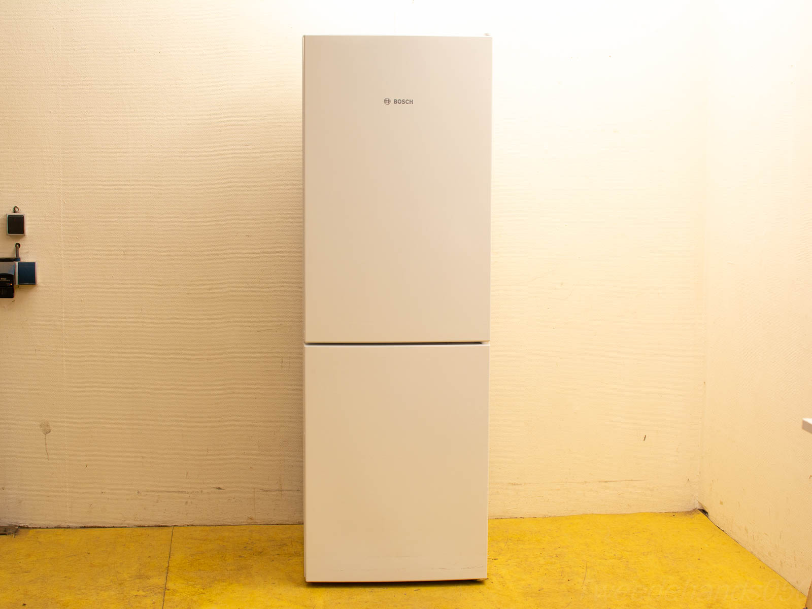 Sleek white Bosch refrigerator in a minimalist kitchen with a vibrant yellow floor.