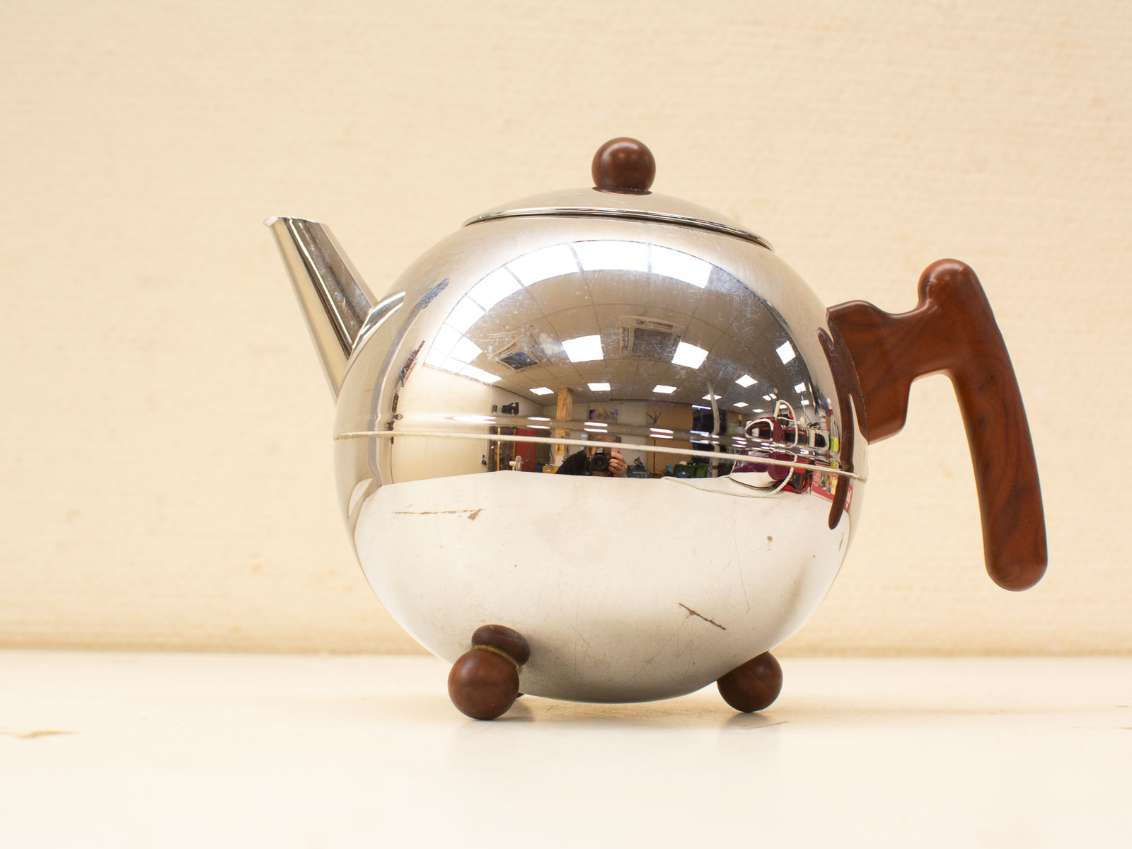 Sleek stainless steel teapot with wooden handle and feet, perfect for stylish tea serving.