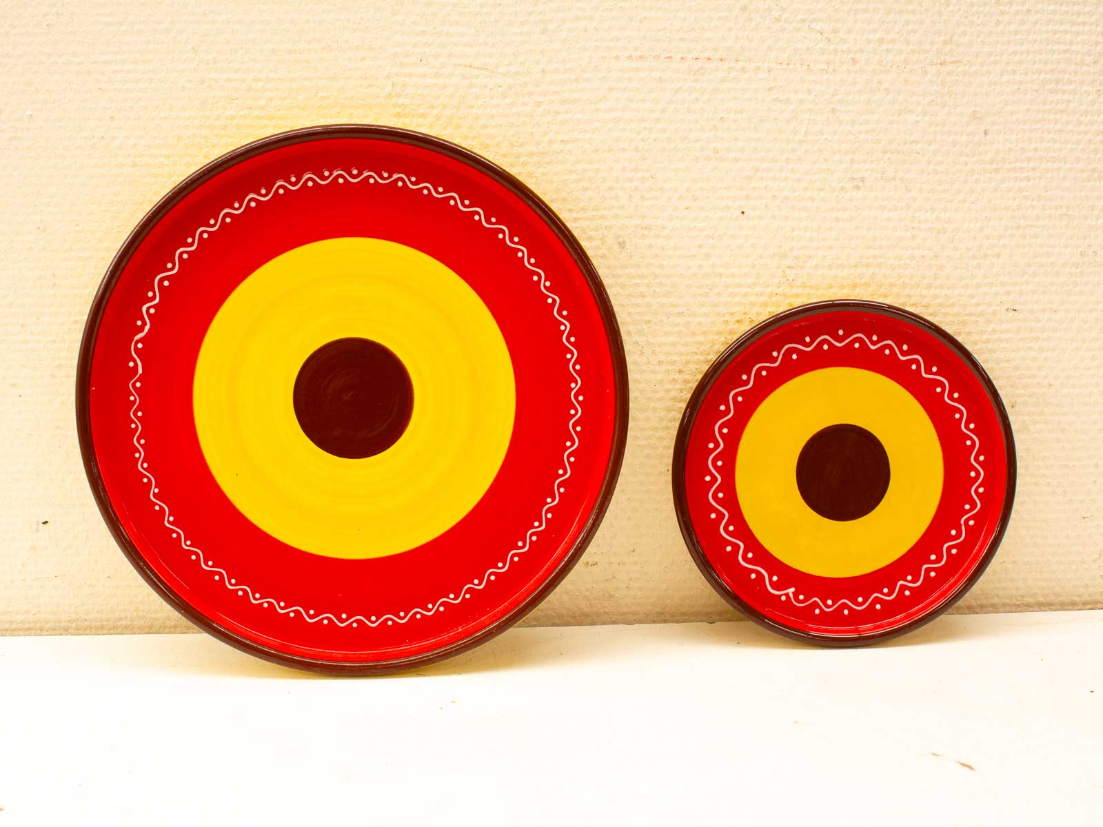 Handcrafted ceramic plates with vibrant concentric patterns in red, yellow, and brown.