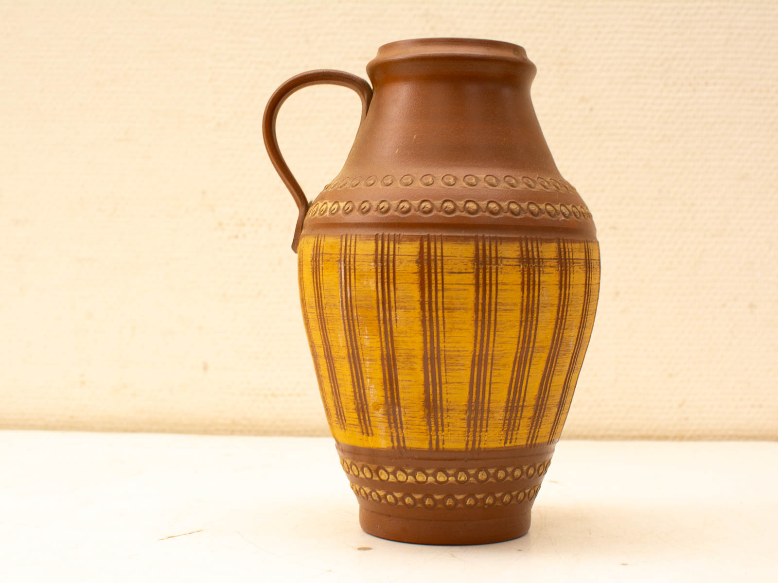 Elegant ceramic jug with earthy tones, intricate designs, and vibrant yellow stripes. Perfect decor.