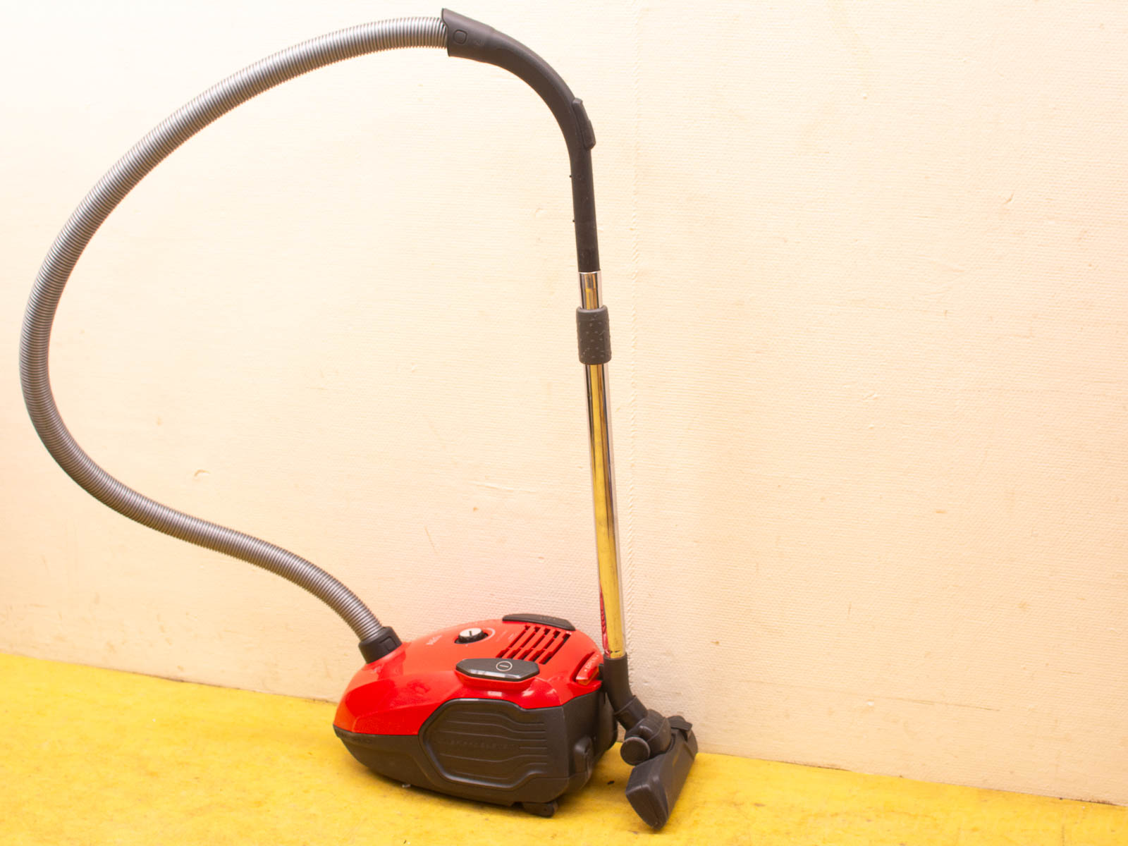 Sleek red vacuum cleaner with a flexible hose and versatile nozzle for efficient cleaning.