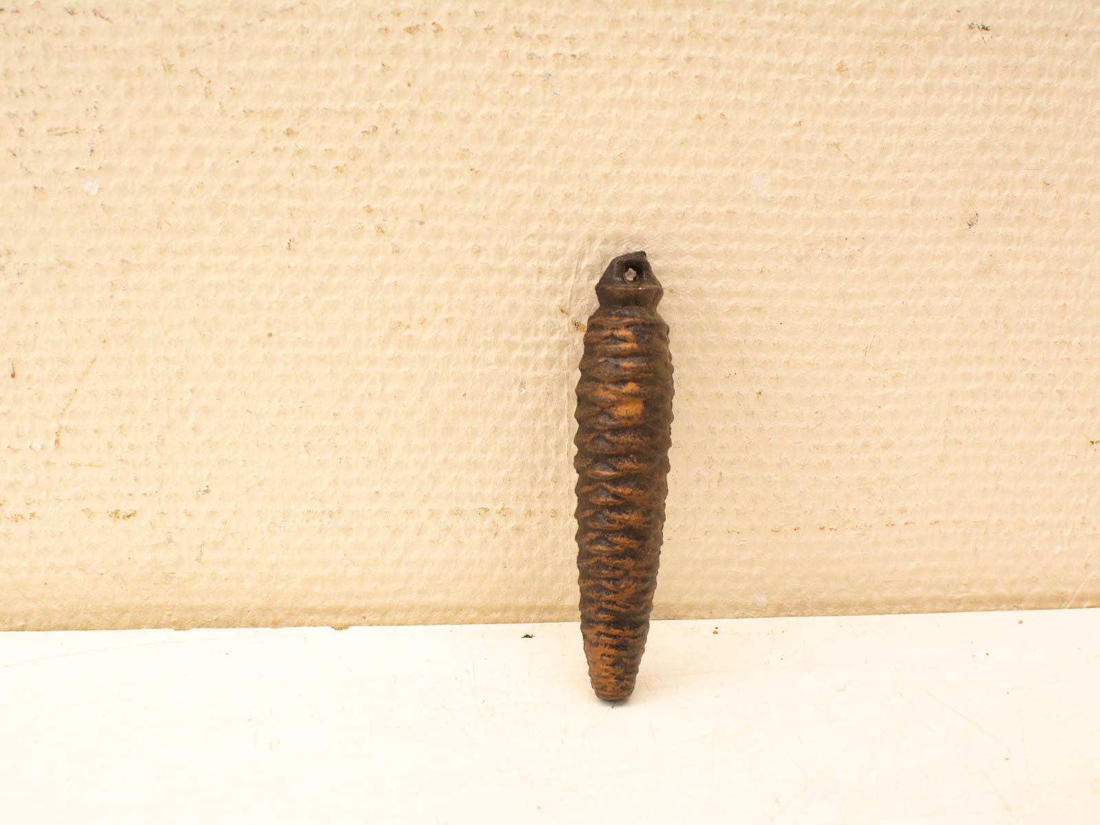 Antique ridged dark-brown metal object against a soft beige canvas background.