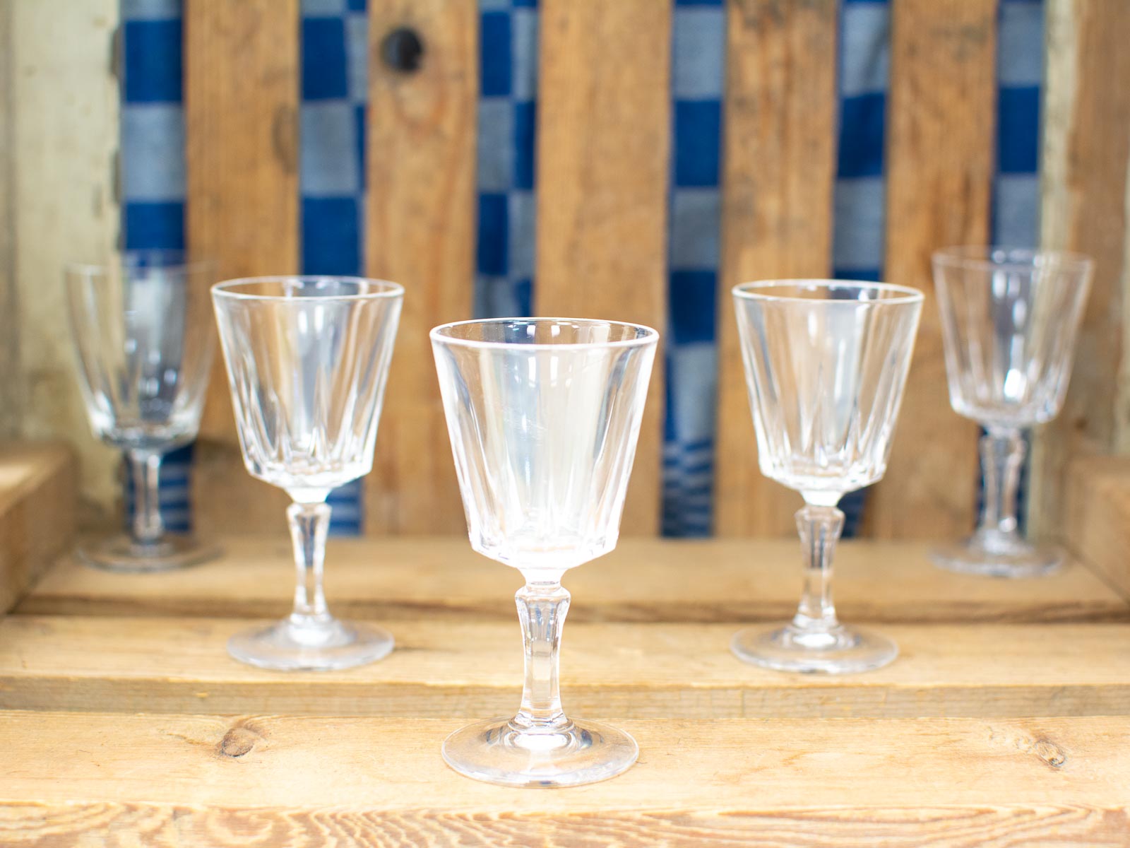 Elegant crystal glasses shine against a rustic wooden backdrop with a hint of blue and white fabric.