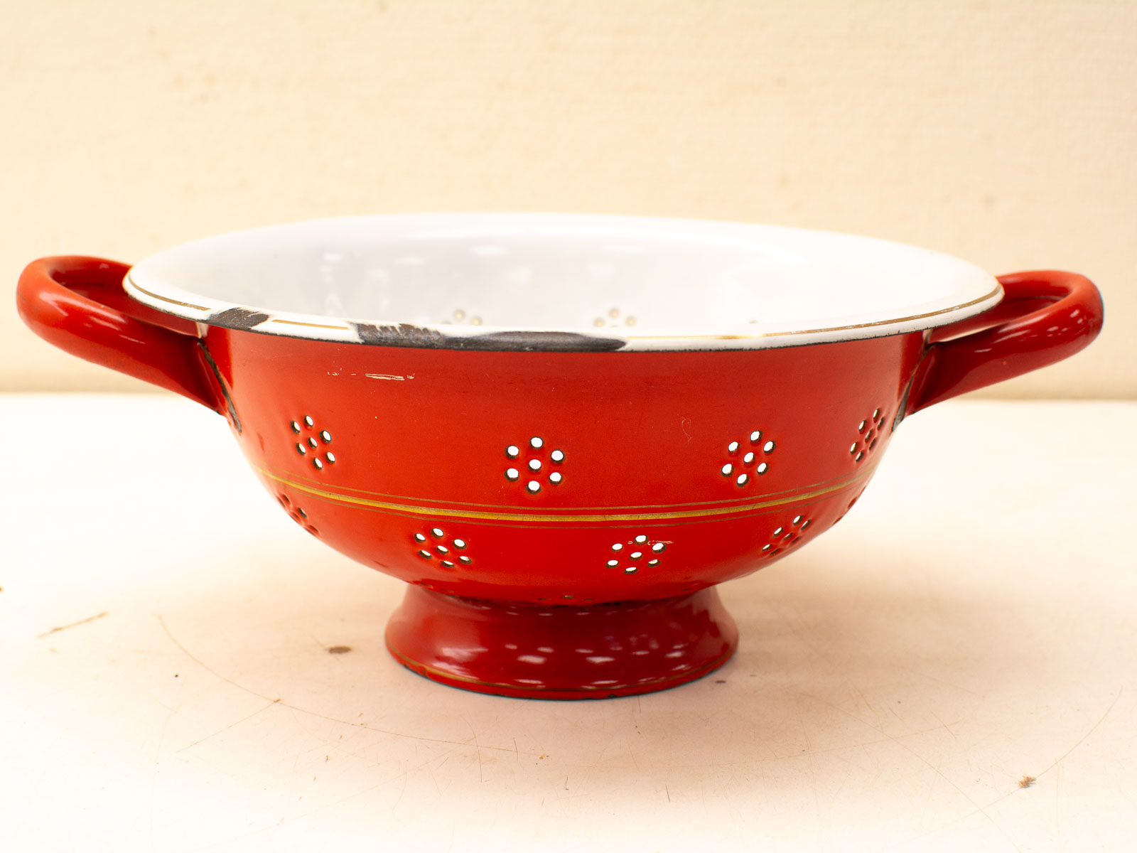 Vintage red enamel colander with gold stripe, perfect for draining pasta and adding charm.